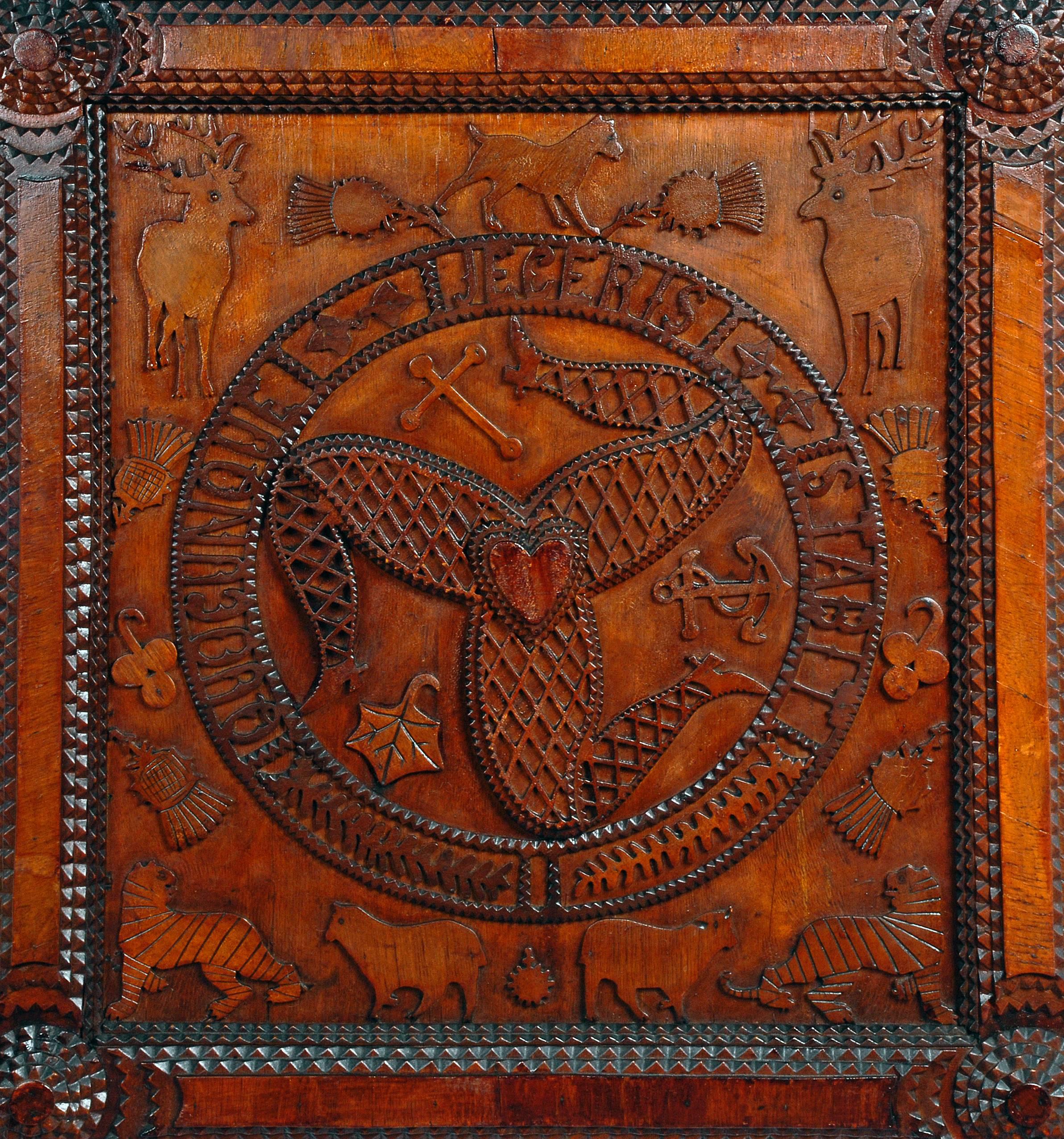 An unusual heavily symbolic tramp art carved plaque depicting the coat of arms of the Isle of Man, with the Latin phrase Quocunque Jeceris Stabit (whichever way you throw it, it will stand), with applied stag, thistle, tiger, Manx (a breed of cat