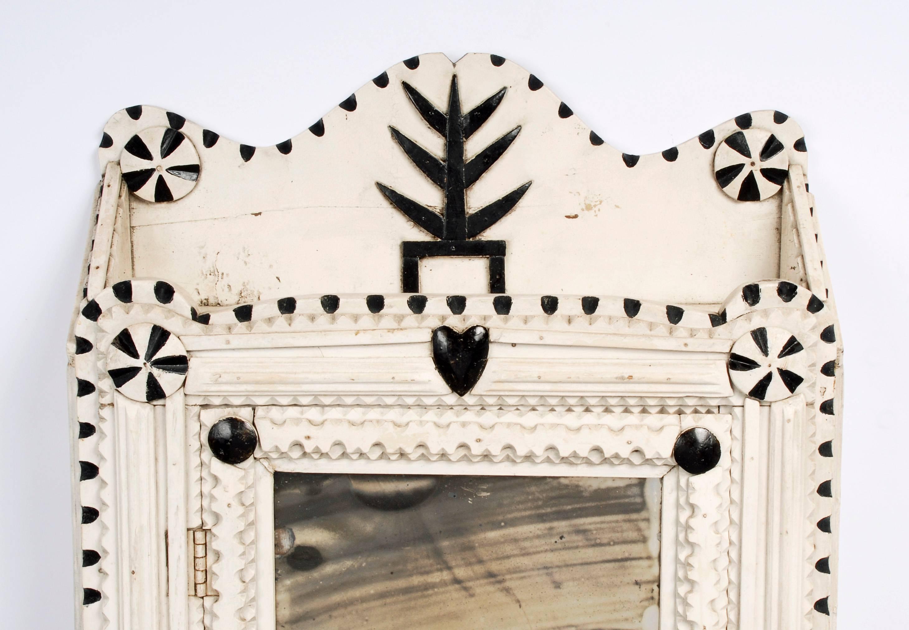 A painted Tramp Art wall cabinet with a central mirror, pinwheels, a heart and a carved tree at its crest. The cabinet held medicines and has interior shelving. Some of the medicines were included in the cabinet. The mirror is original and you can