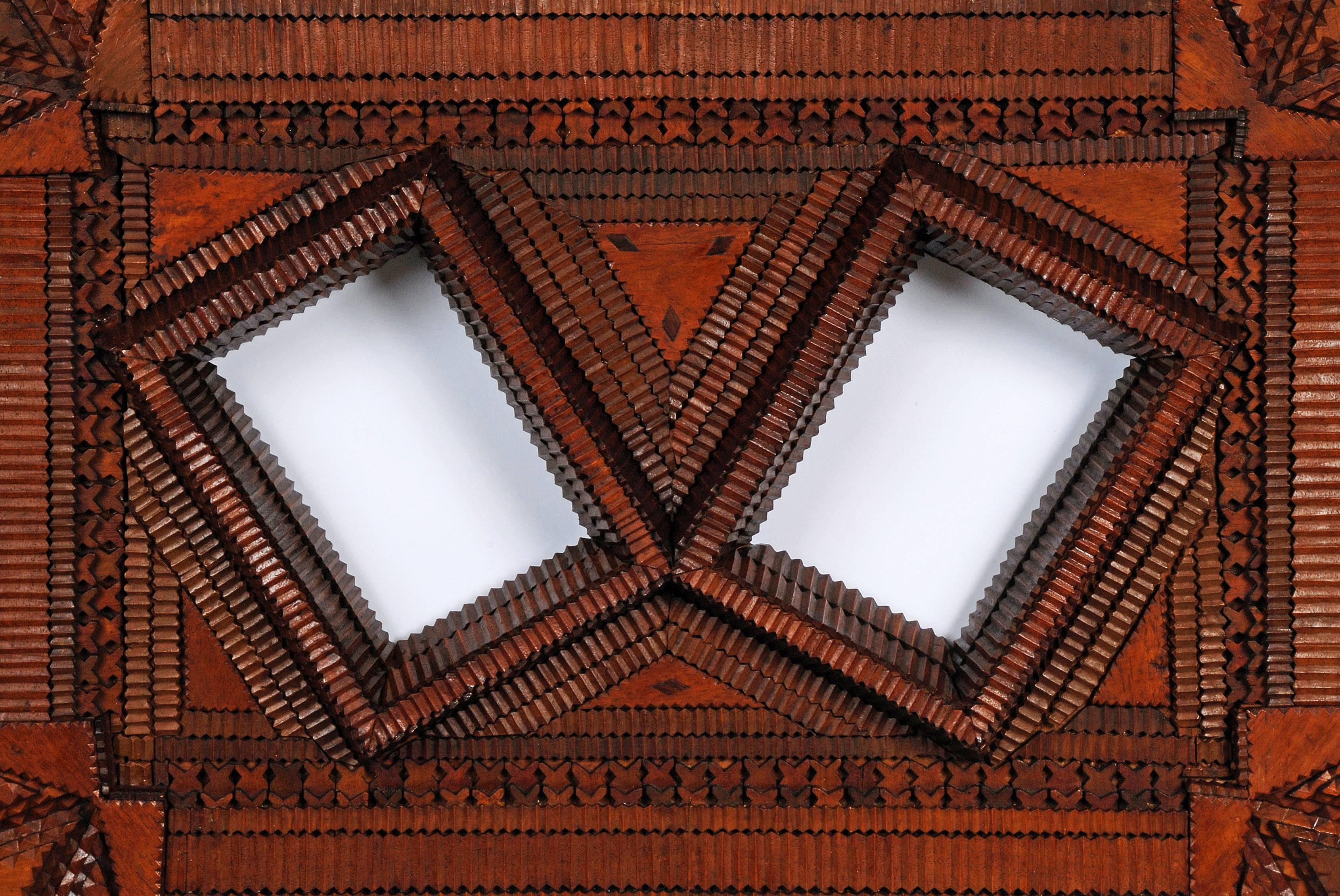 A heavily detailed Tramp Art double portrait frame in the John Zubersky style with floral corners and tulip edges. The frame exhibits hundreds of individually carved pieces applied to a wooden canvas. The openings are raised making a platform to