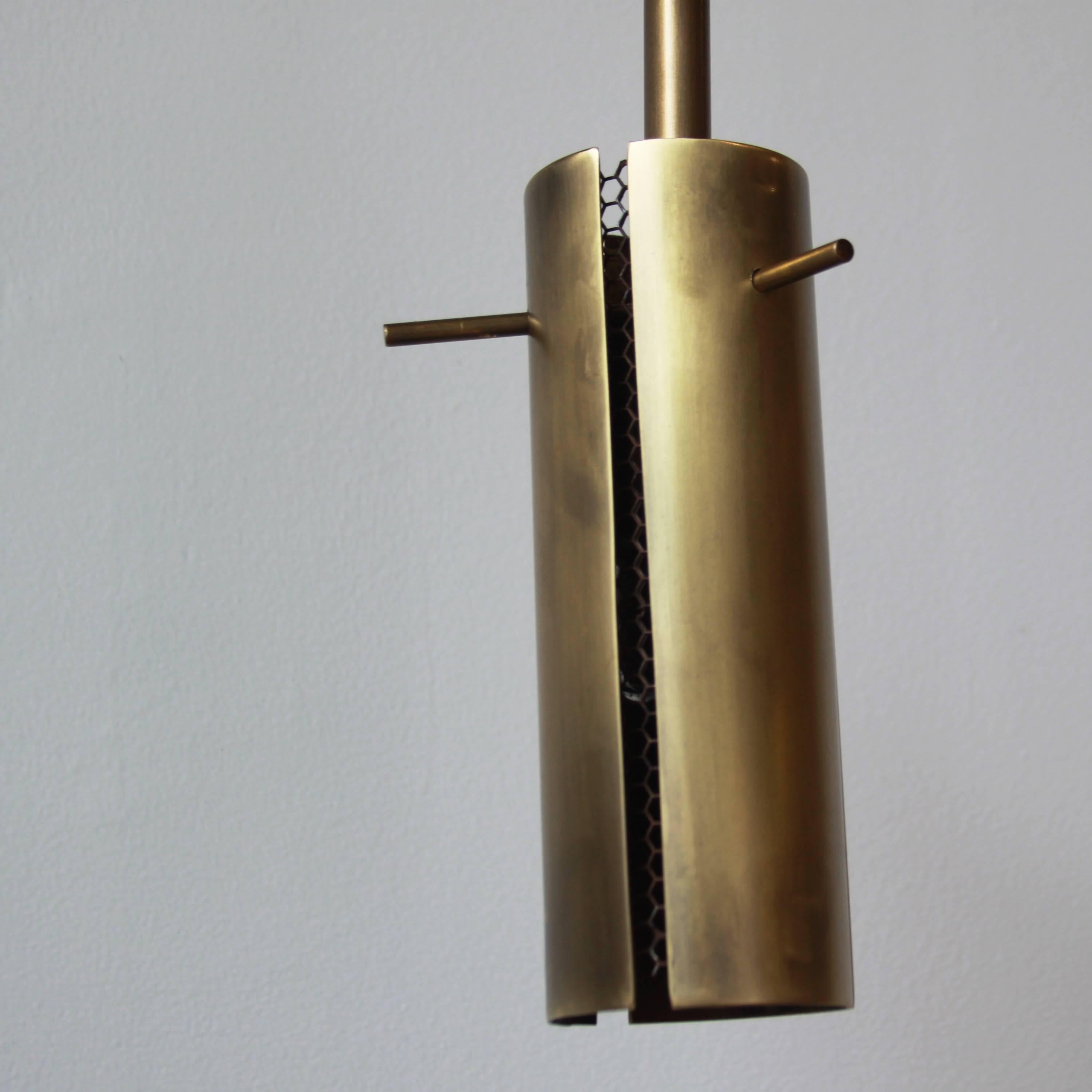 This elegant brass pendant light by Thomas Hayes studio provides DIM directional lighting. This linear fixture's slow rotation provides a warm glow and is available in steel as well as a variety of brass finishes.