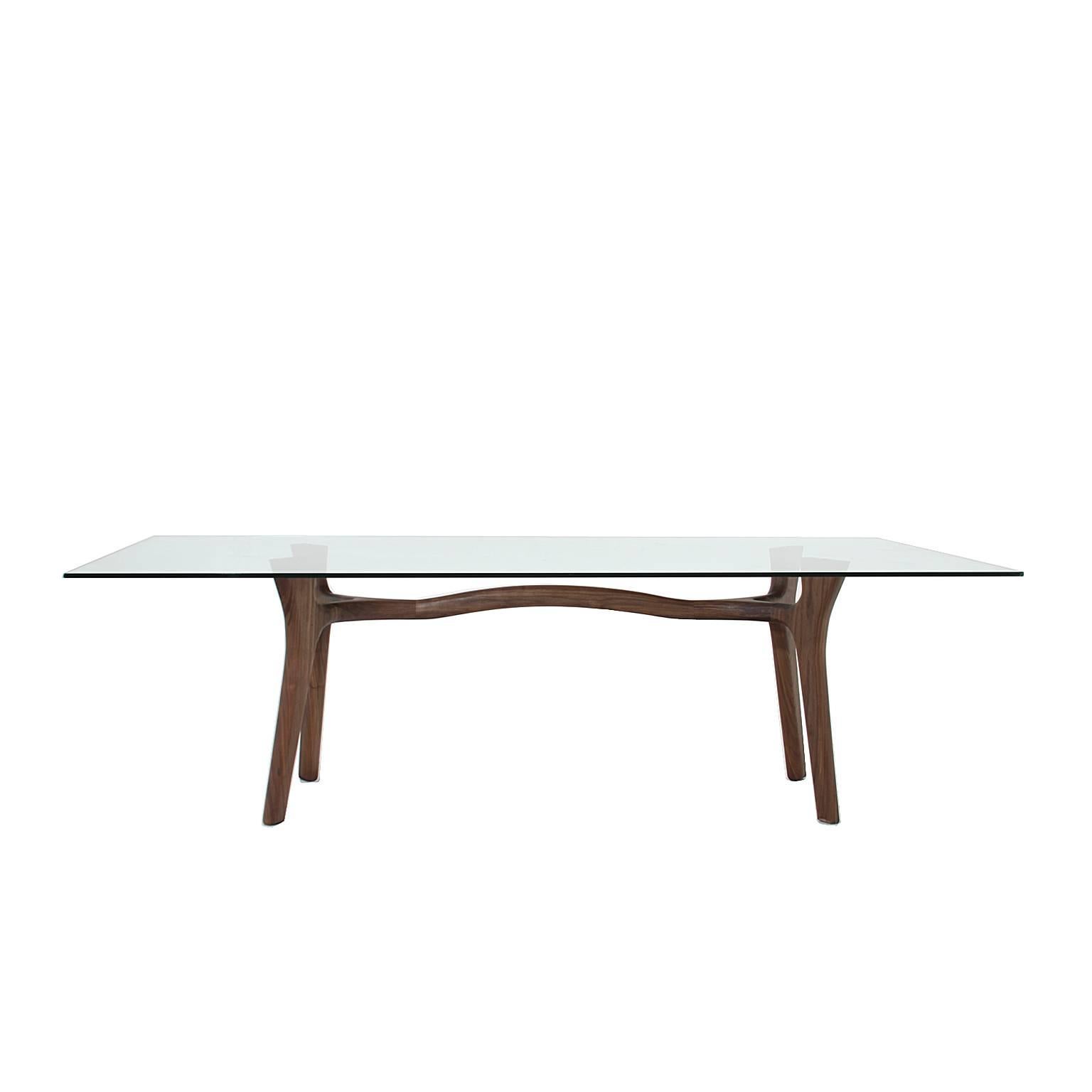 A sculptural solid walnut dining table with an arched center and a floating glass top inspired by the designs of Italian born Giuseppe Scapinelli from Brazil. Glass top width 100