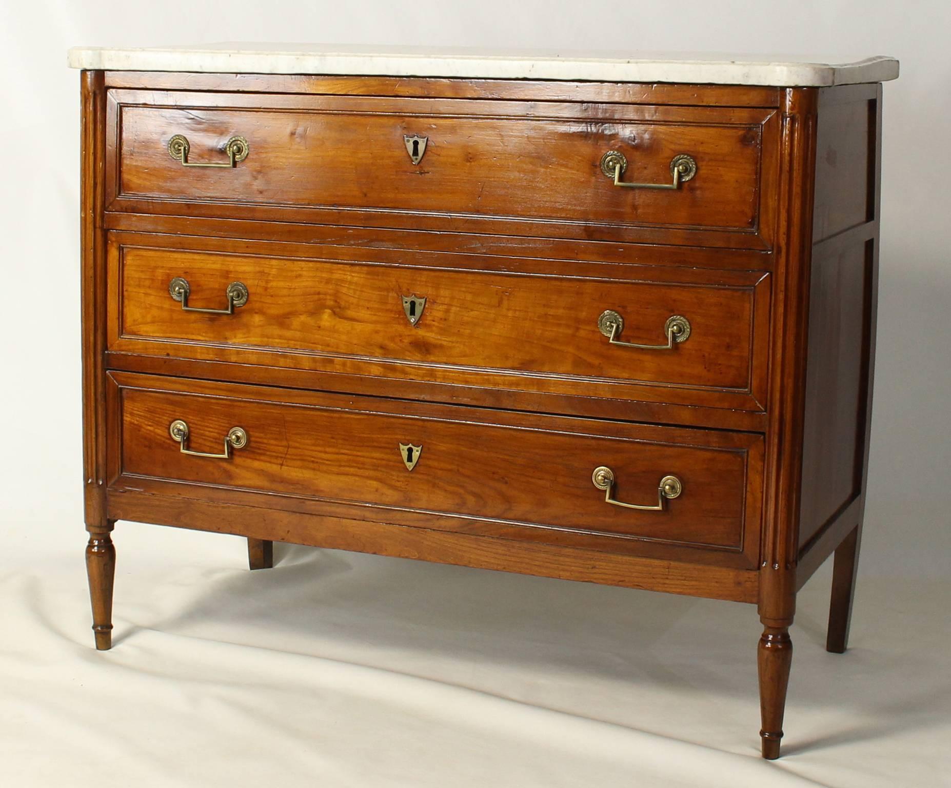 A fine early 19th century French three-drawer Directoire commode with brass rectangular handles flanked on either side by fluted column corners raised on turned tapering front legs retaining its original mellow white marble top.