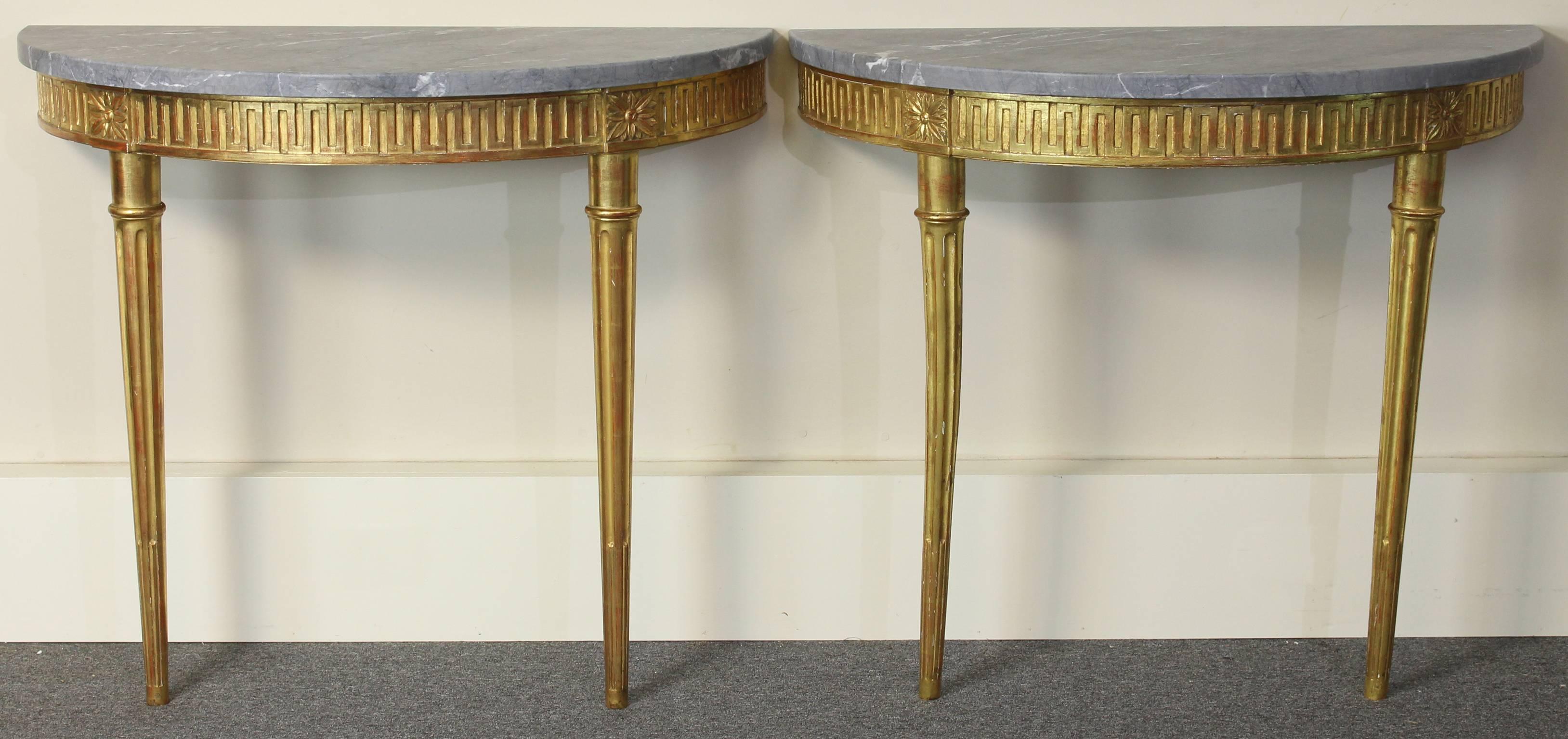A magnificent pair of French Directoire carved and water gilt decorated wall-mounted demilune console tables with elegant Greek key decoration on the apron and large fluted column tapering legs.