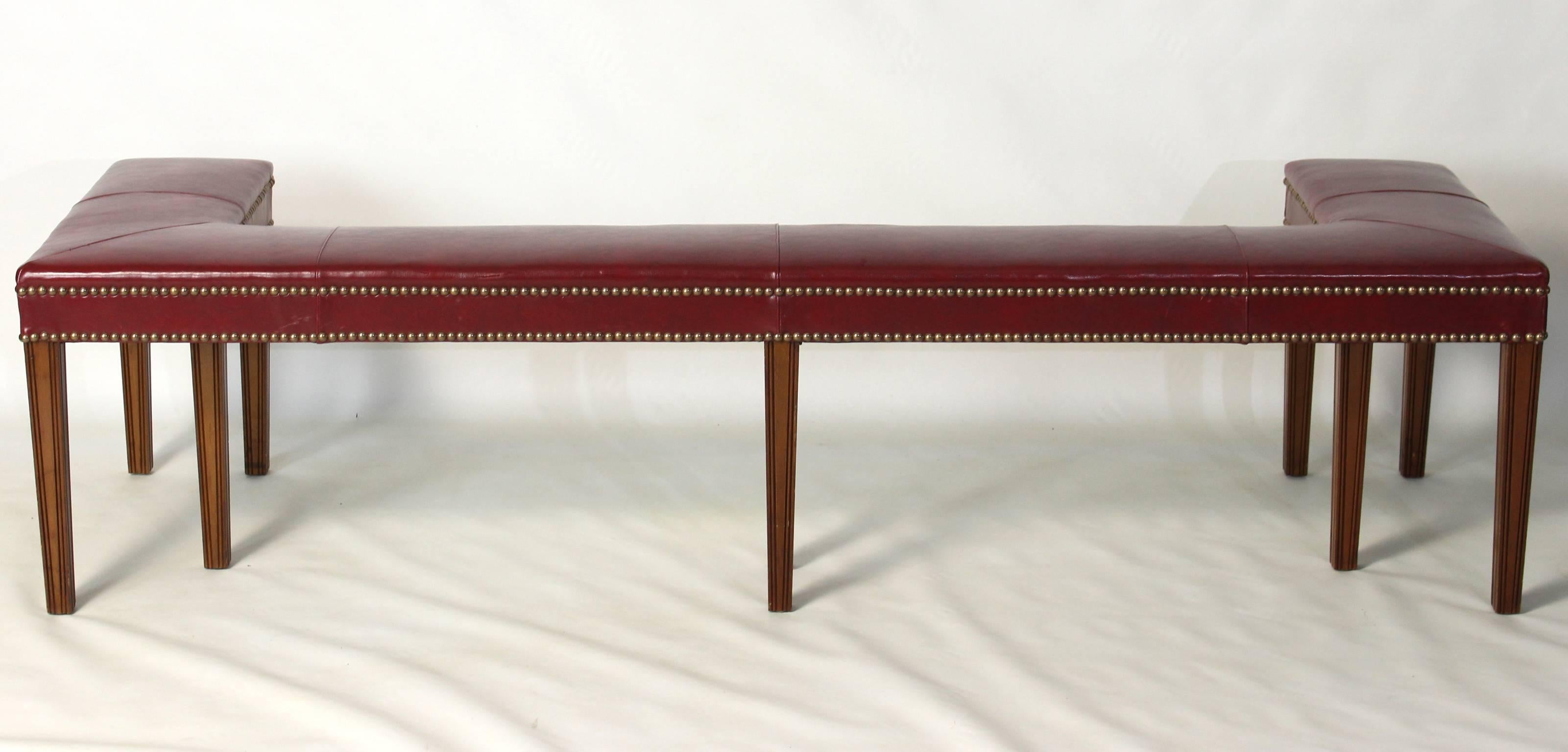 A Regency style red leather covered fire fender or bench accented with brass tacks and resting on reeded square tapering mahogany legs.