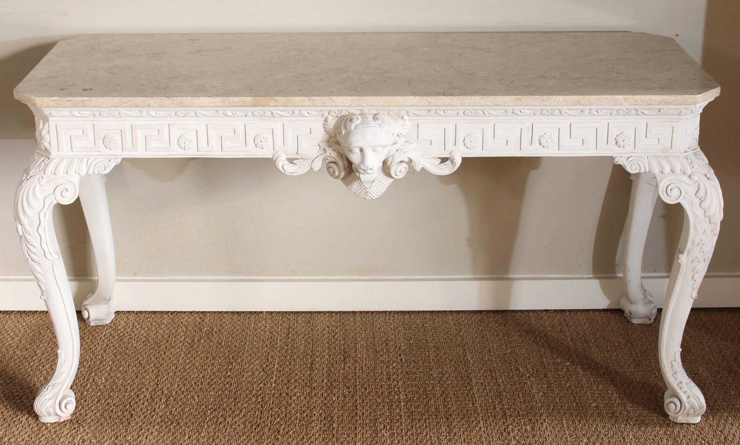 A beautifully carved and painted George III style console table with a mellow, pale cream colored marble top. The Greek key carved apron on all four sides accented with large lion's head on the front. Carved acanthus leaf decorated cabriole legs