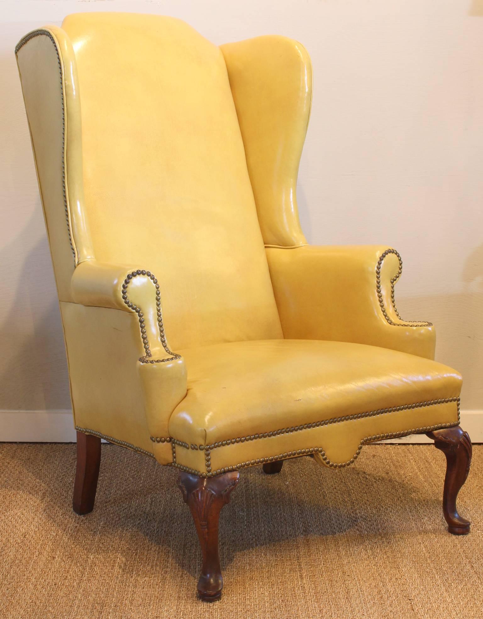 A delightful 1940s stylized Georgian wing chair with an unusually tall back in its original mustard yellow leather upholstery accented with brass nailheads.