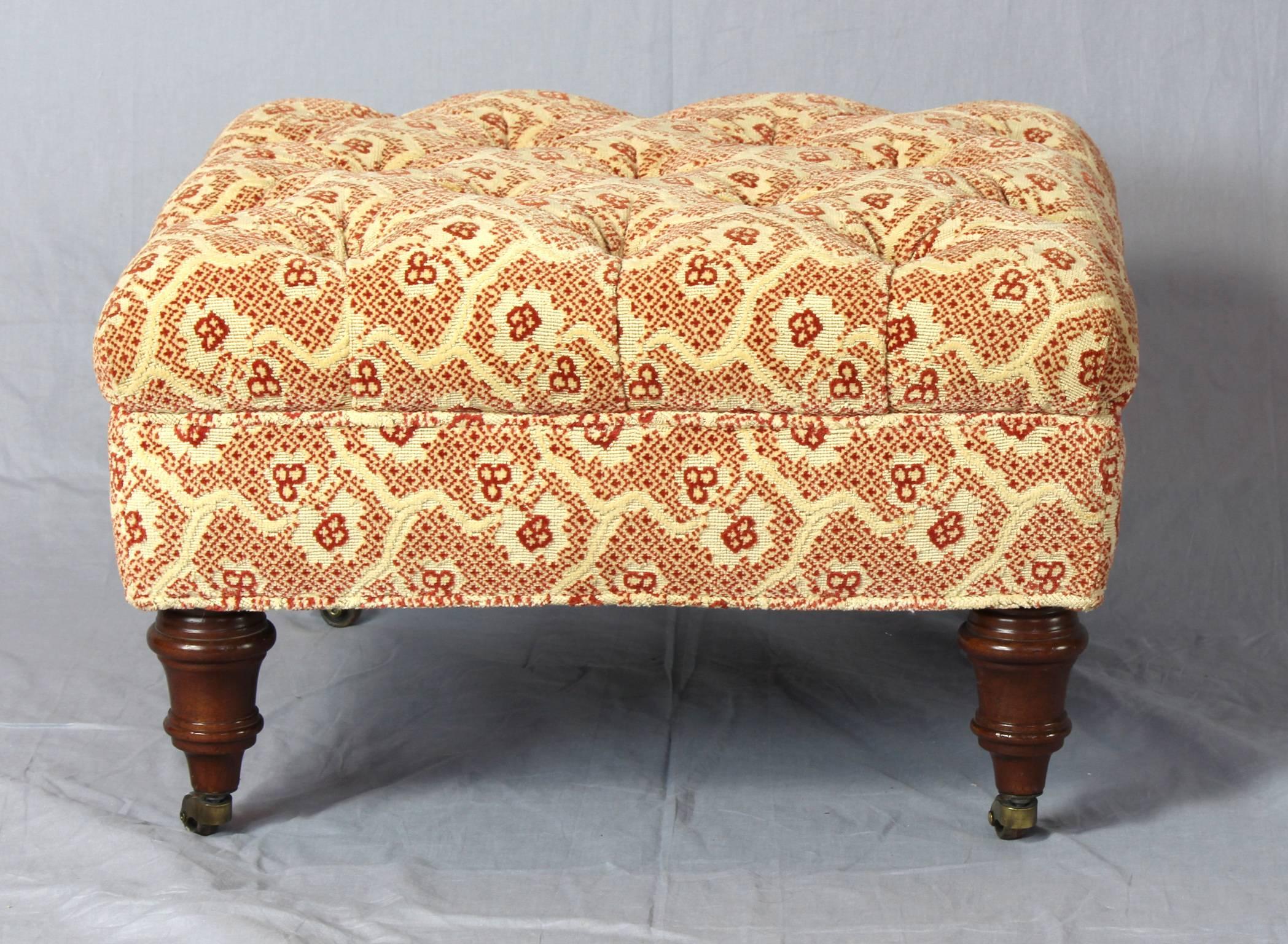 A diminutive buttoned upholstered footstool or ottoman on turned wooden legs terminating in brass casters.