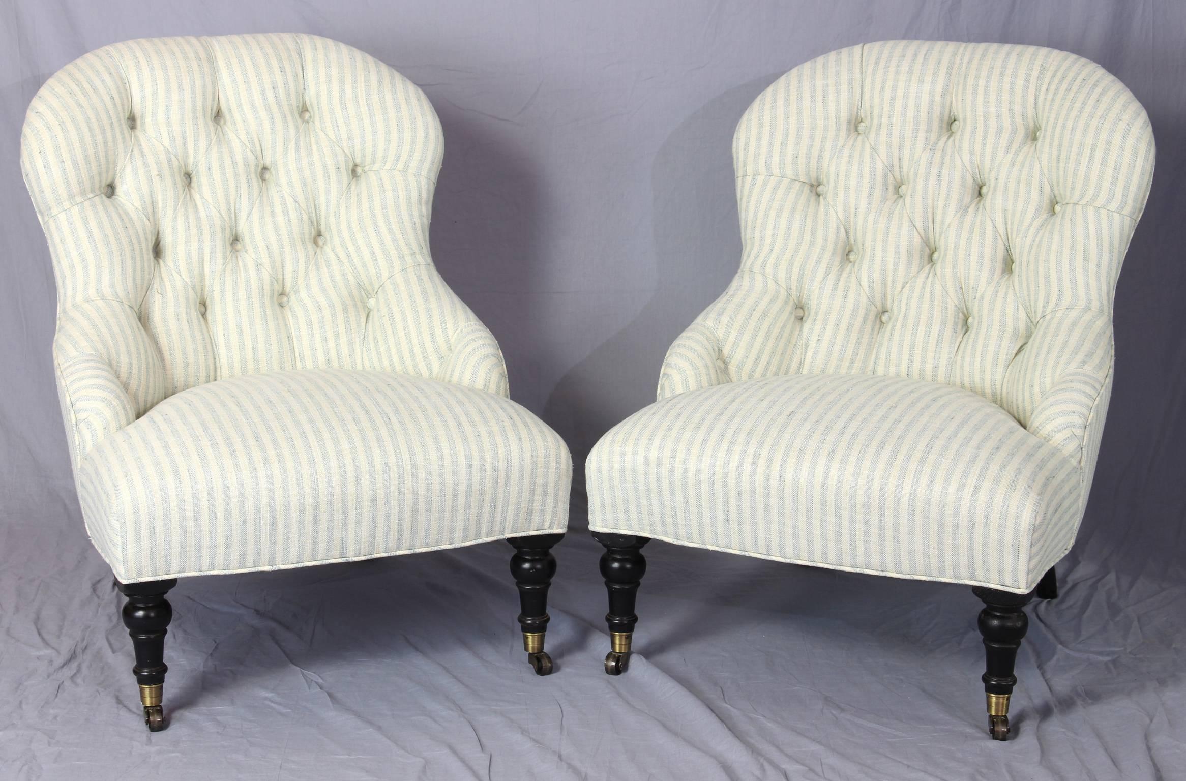 A pair of Edwardian style buttoned back slipper chairs on turned front legs with brass casters newly upholstered in a cream and blue striped linen/cotton fabric.