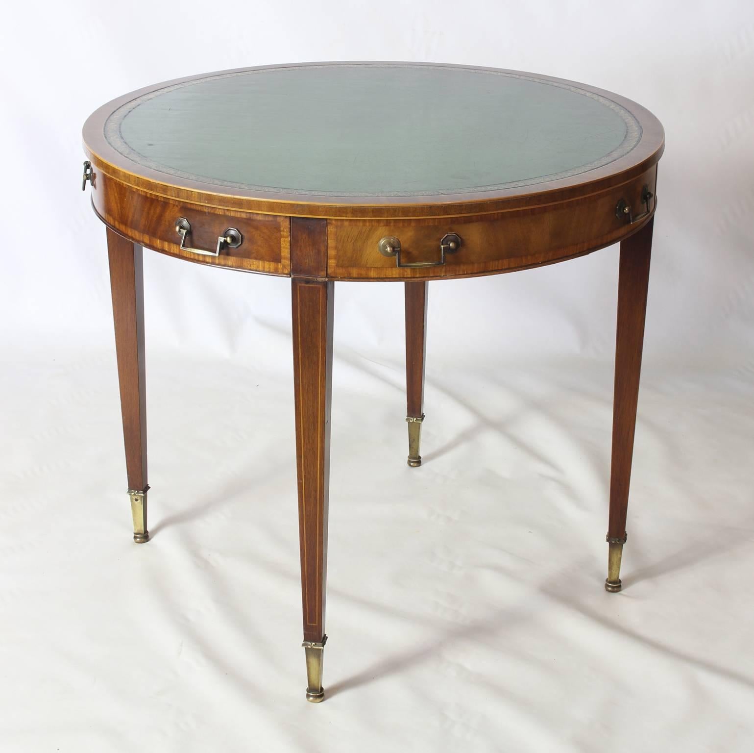 An elegant early 20th century Regency style green leather top drum table with three simulated and one real drawers resting on four square tapering legs terminating in brass cast feet.