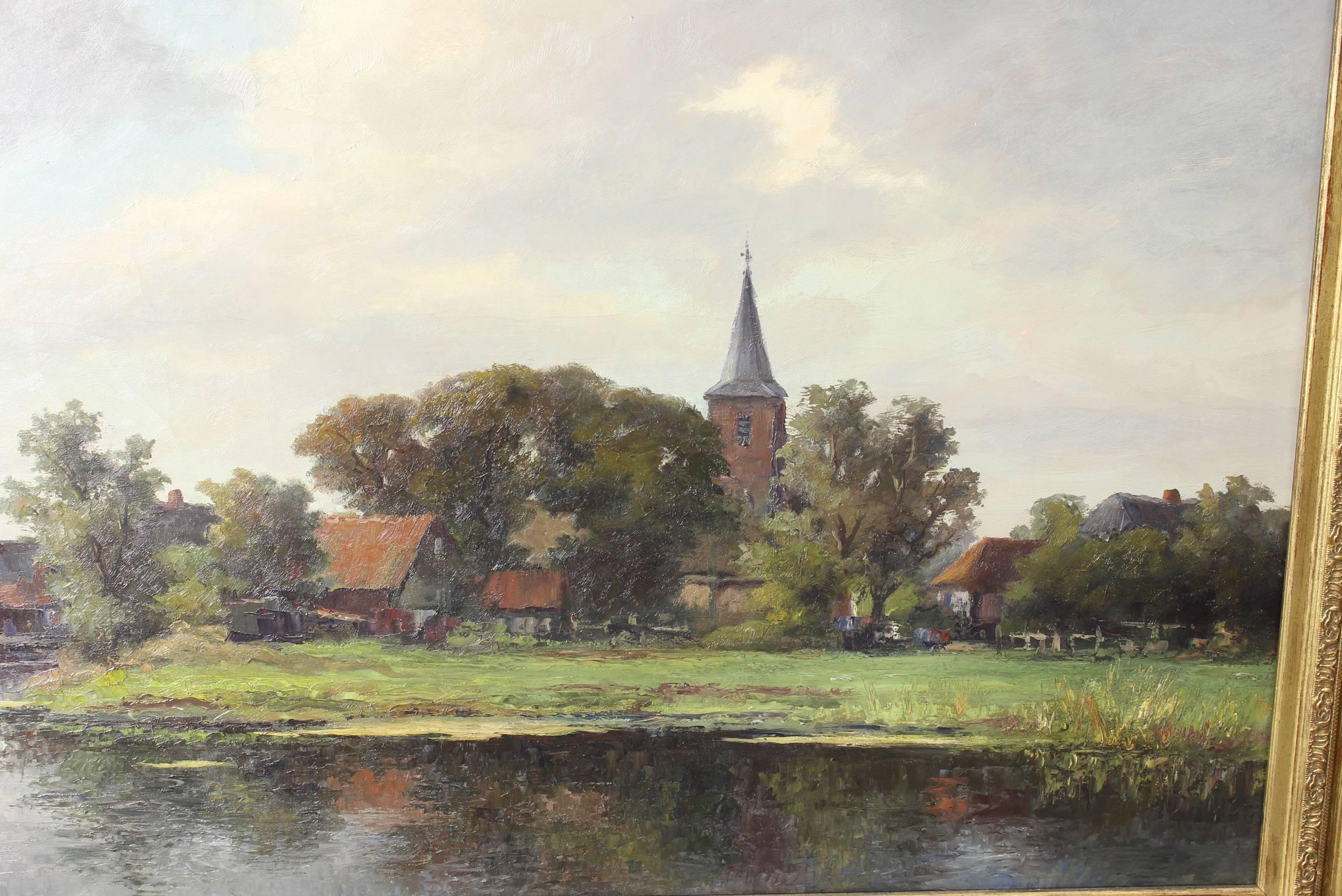 A beautifully painted and exceptionally large early 20th century oil on canvas Dutch painting of a waterfront landscape with a church steeple and windmill in the background in an elaborate giltwood frame. Signed lower left.
