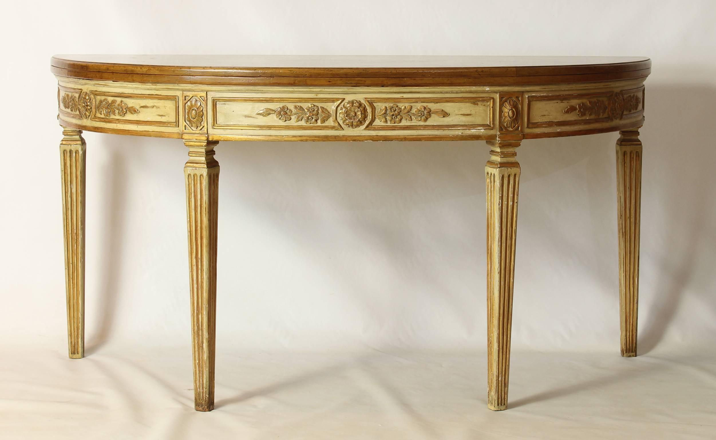 A large and unusual custom designed Italian neoclassical style demilune fold-over console table that converts into a dining table. The solid pecan wood top over an elaborately carved and painted apron resting on four square tapering fluted legs. The