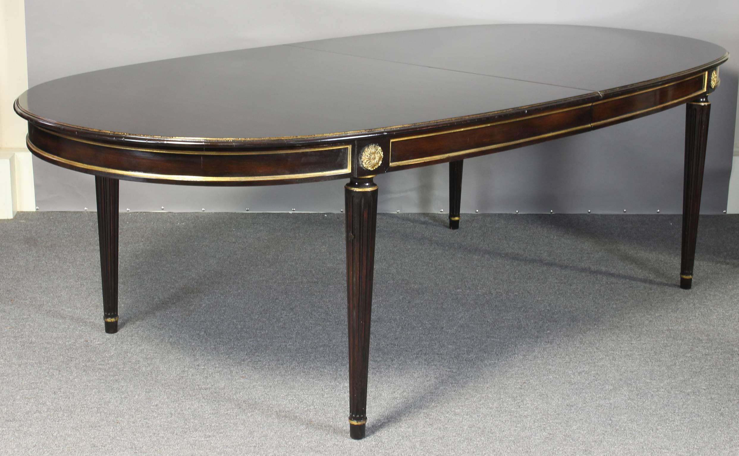 A mid-20th century Louis XVI style two leaf dining table in the manner of Maison Jansen. The hand rubbed French polished and ebonized top is supported by elegant, round fluted tapering legs.