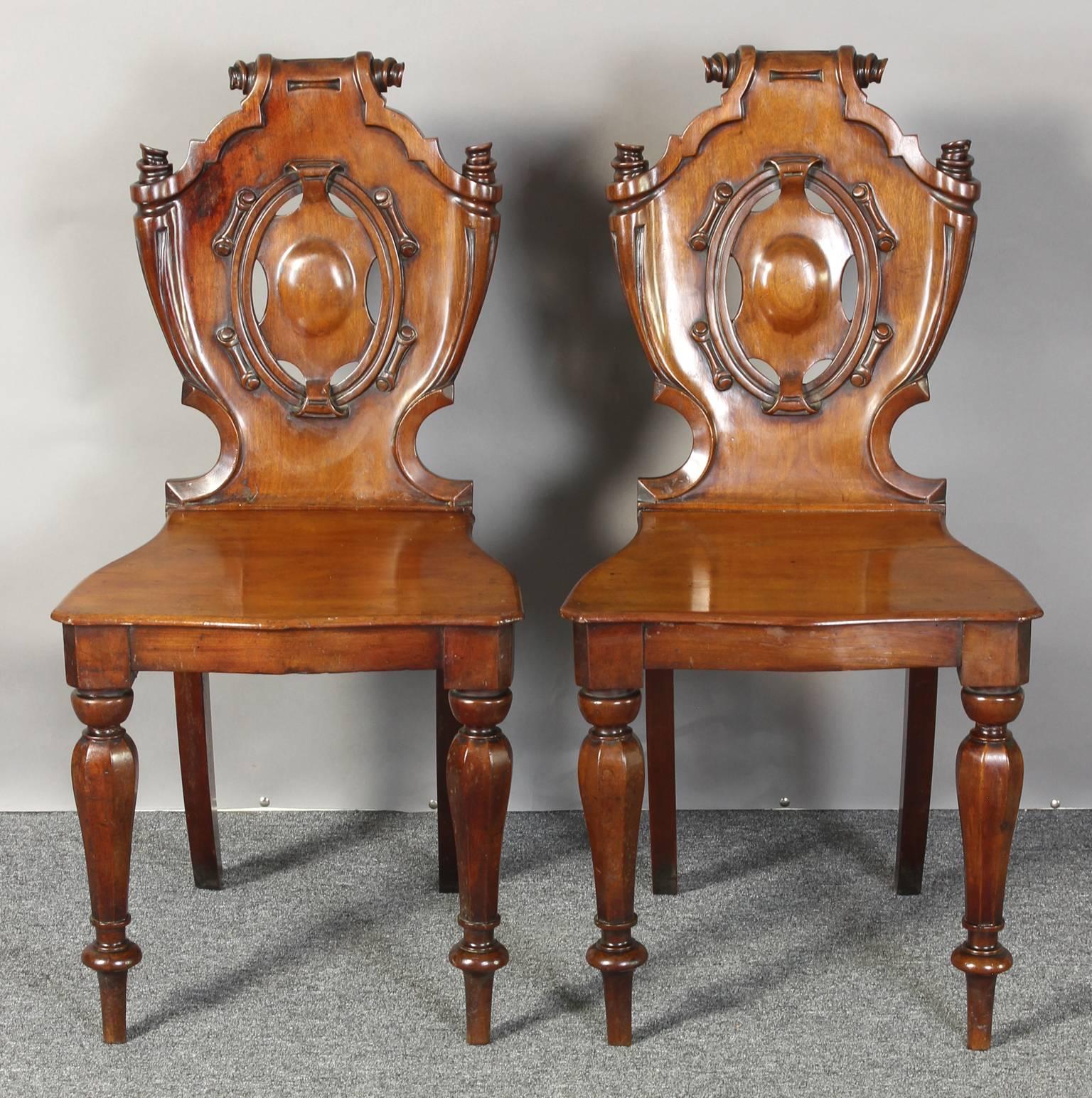 A fine pair of English William IV period mahogany hall chairs with heavily carved cartouche shaped backs and plank seats supported on turned tapering legs.