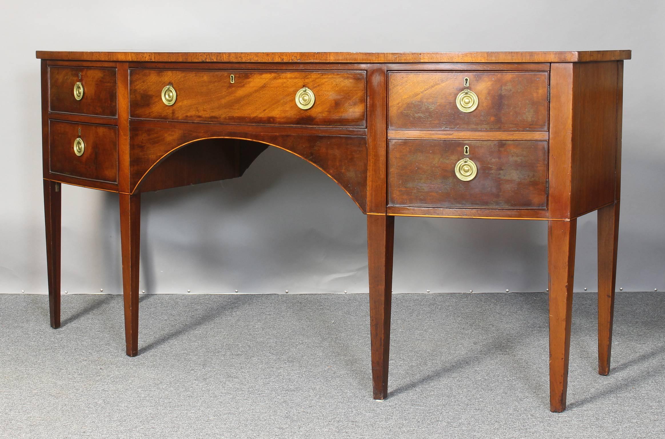 A large and impressive George III style bow fronted mahogany sideboard dating from the early 20th century. with three drawers and a cabinet door resting on square tapered legs.