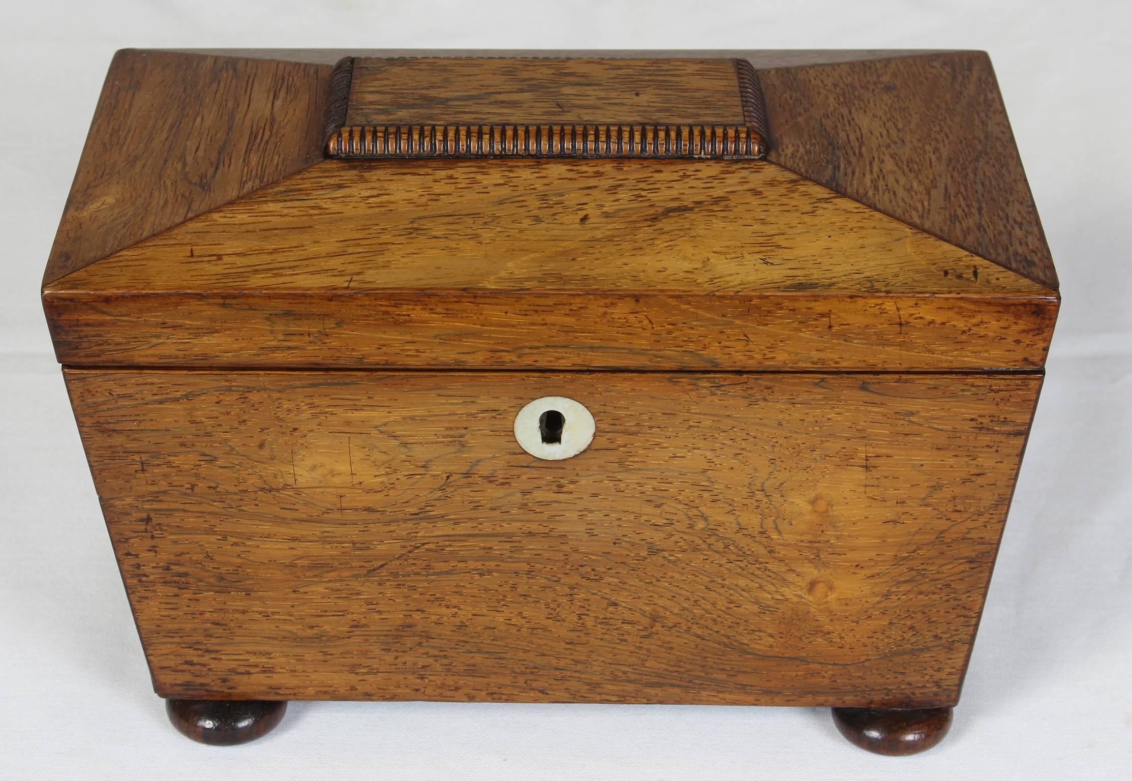 An elegant early 19th century. English sun-faded mahogany tea caddie in the shape of a sarcophagus with mother-of-pearl escutcheon on bun feet.
