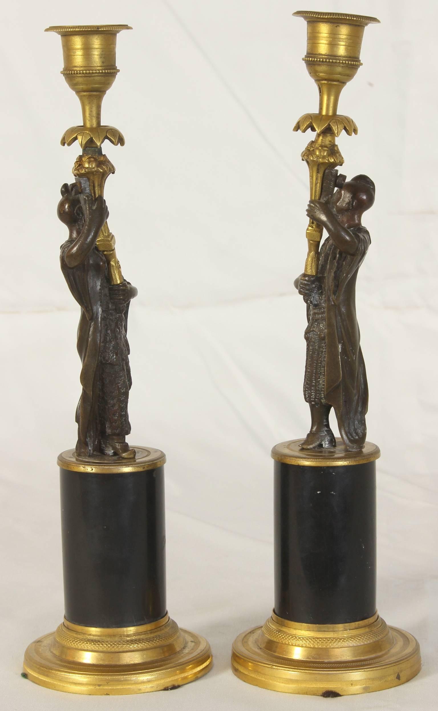A fantastic pair of early 19th Century French gilt and patinated cast bronze Chinoiserie figural candlesticks on black marble cylindrical bases.
