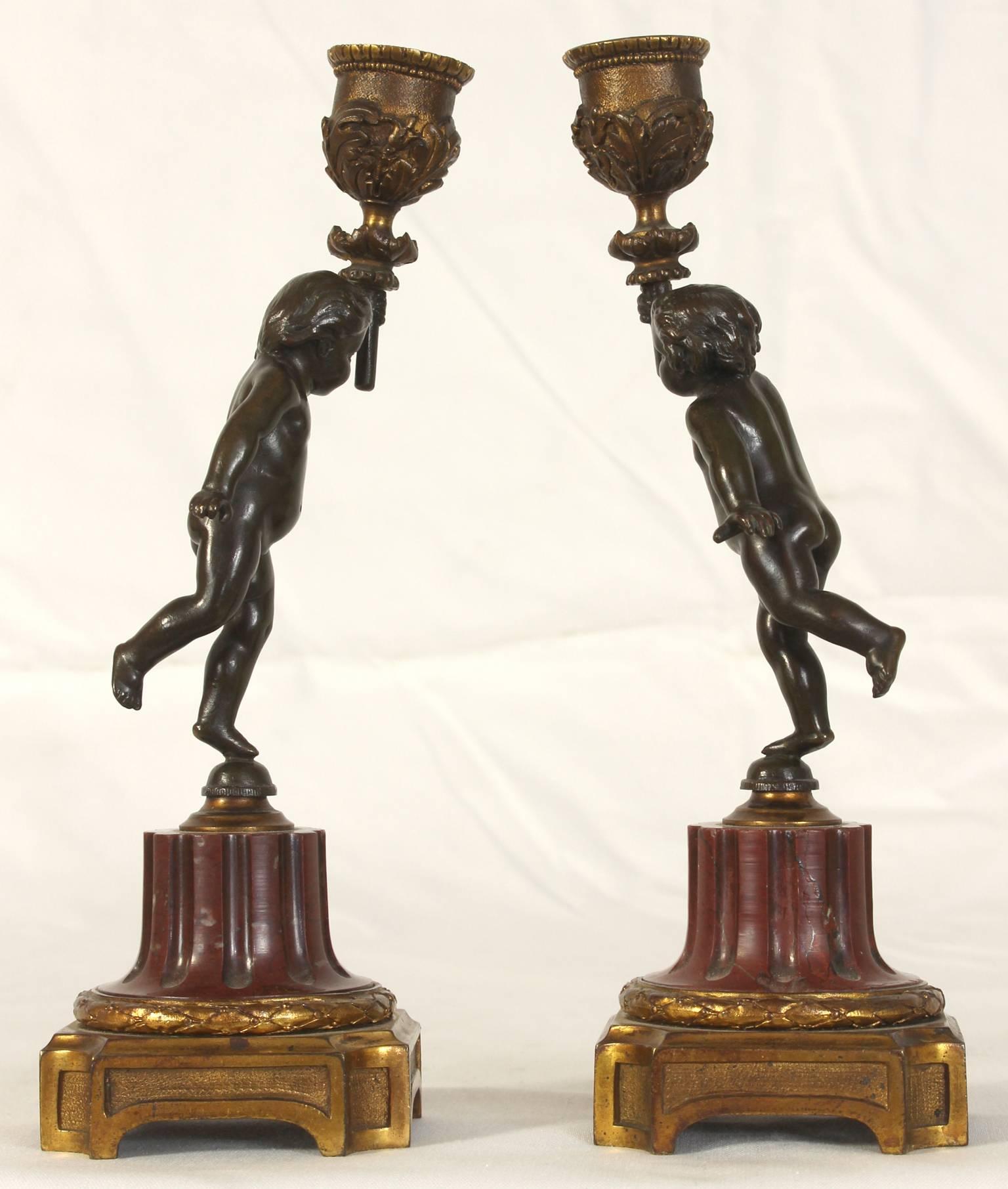 A delightful pair of late 19th Century French cast bronze candlesticks depicting cherubs on rose marble bases.