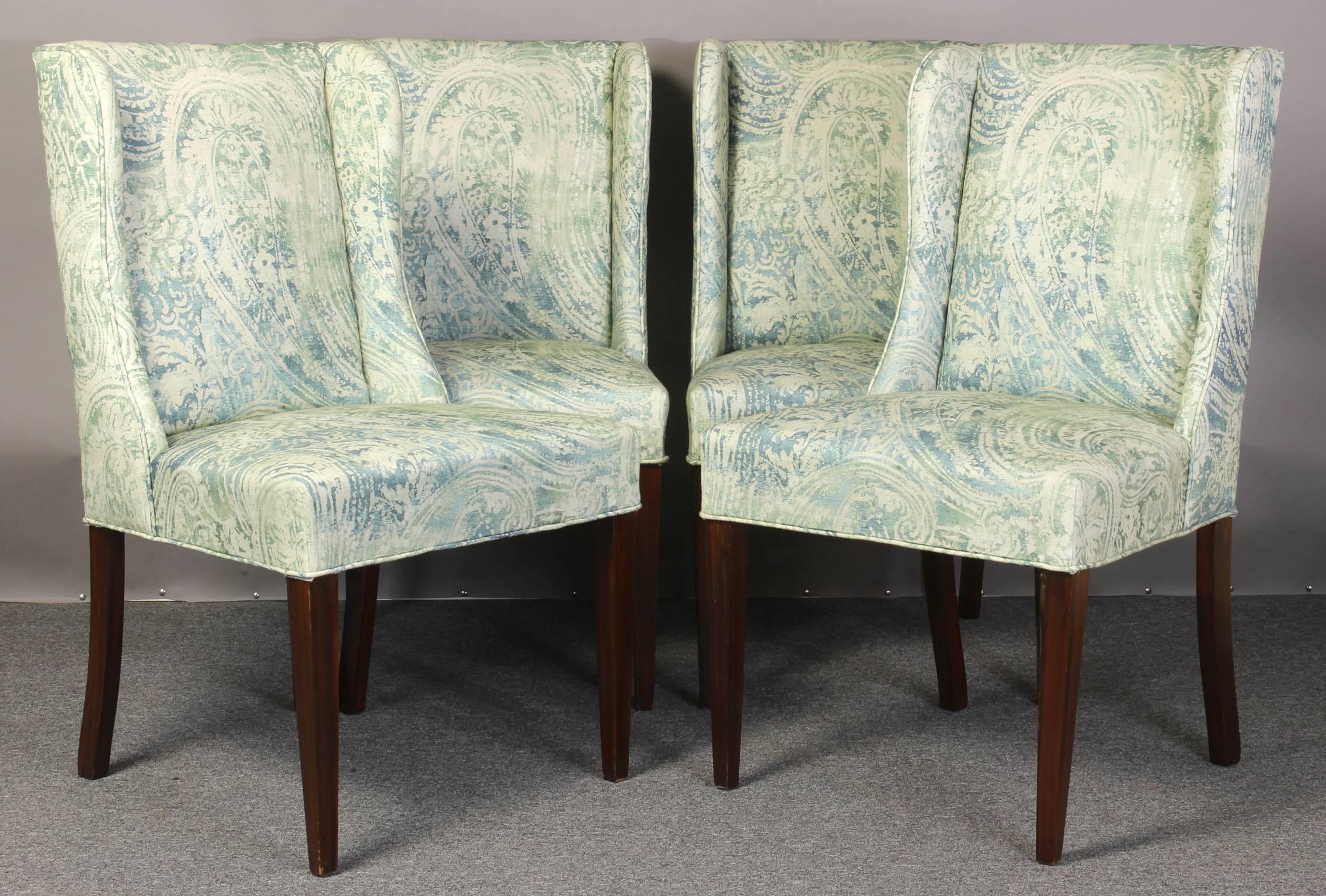 A set of four mid-20th century upholstered stylized wingback dining chairs newly covered in a soft blue-green Italian linen fabric with faux wood grain painted square tapering legs. Would make sensational games table chairs.