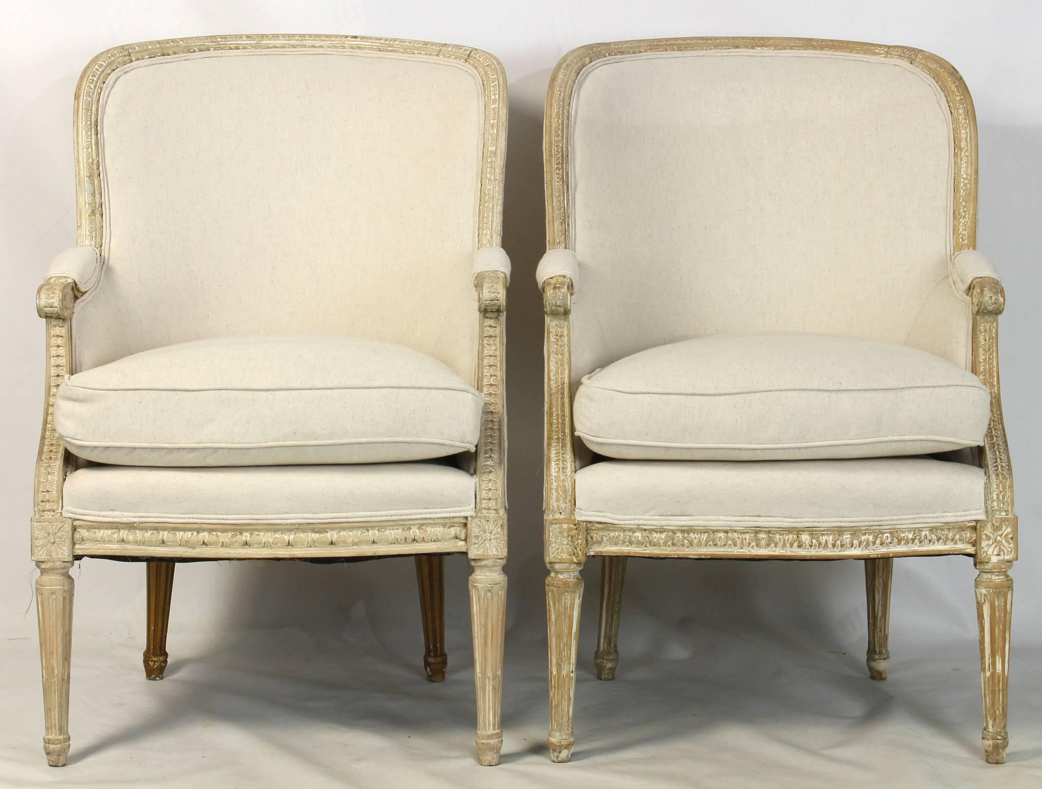 A pair of early 19th century French Louis XVI style bergeres or armchairs in grey cotton fabric, the original painted surface has been removed to reveal the wood grain and elegant detailed carving.  