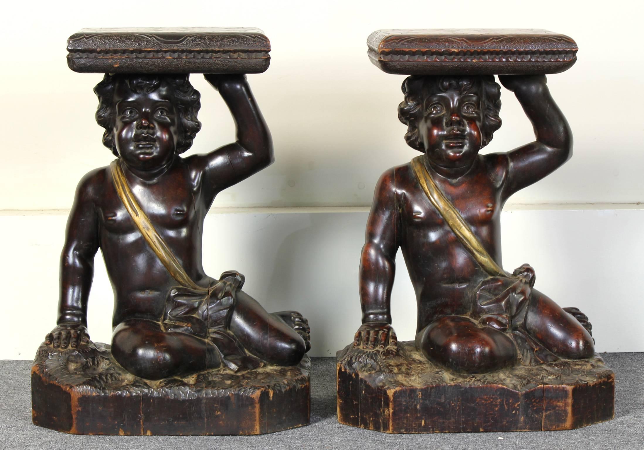 A delightful pair of late 19th C. Italian carved wood side or occasional tables depicting playful cherubs reclining on rocks balancing cushions on their heads. Each piece is unique and charming.  
