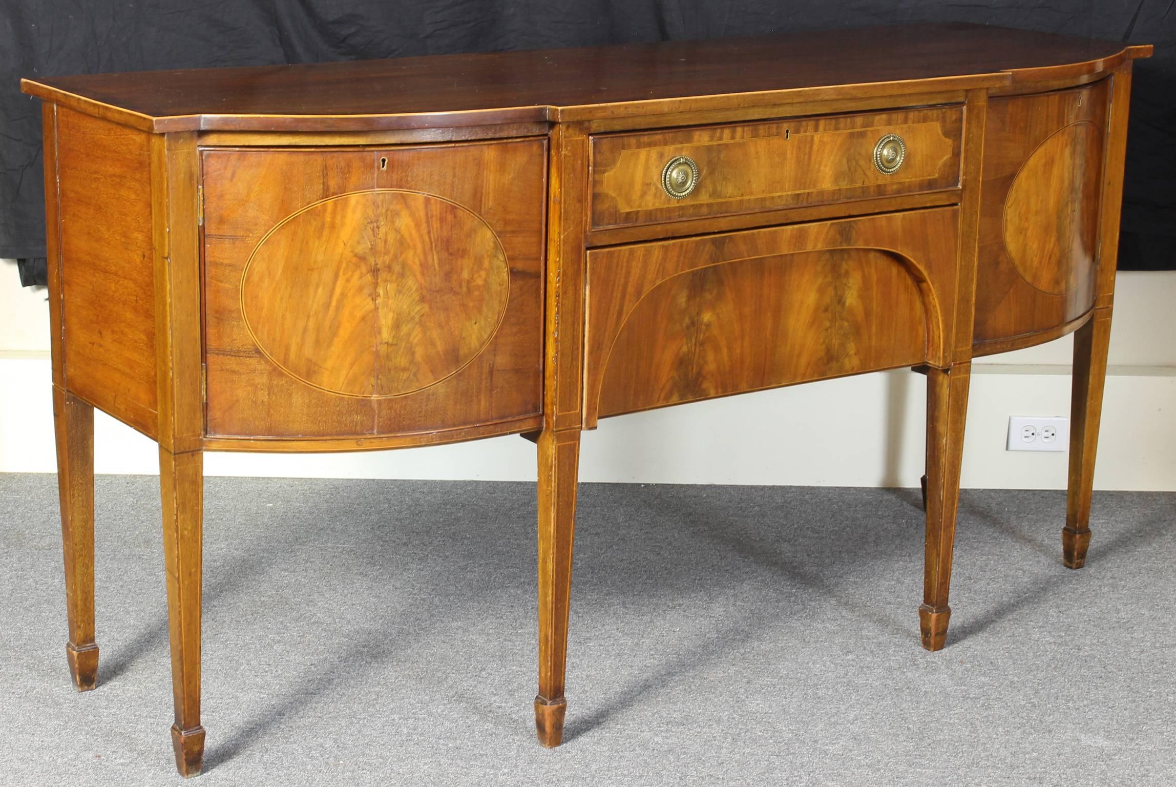 A late 19th C. English mahogany and satinwood sideboard in the Hepplewhite style. The single drawer flanked by two cabinet doors with a concealed lower drawer supported on square tapering legs terminating in spade feet. 