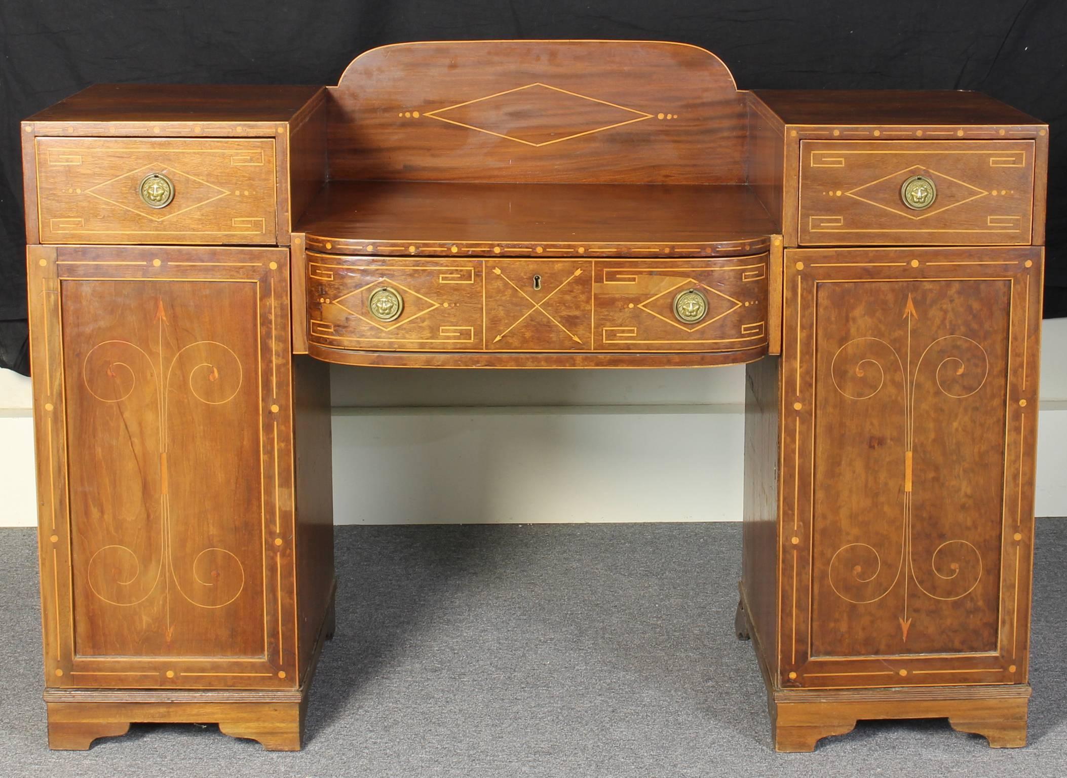 An exceptional Regency mahogany sideboard with extensive satinwood cross banding. The three drawers, each lined with green baize silver cloth over two pedestal doors. This piece displays very fine original lion's head pulls.