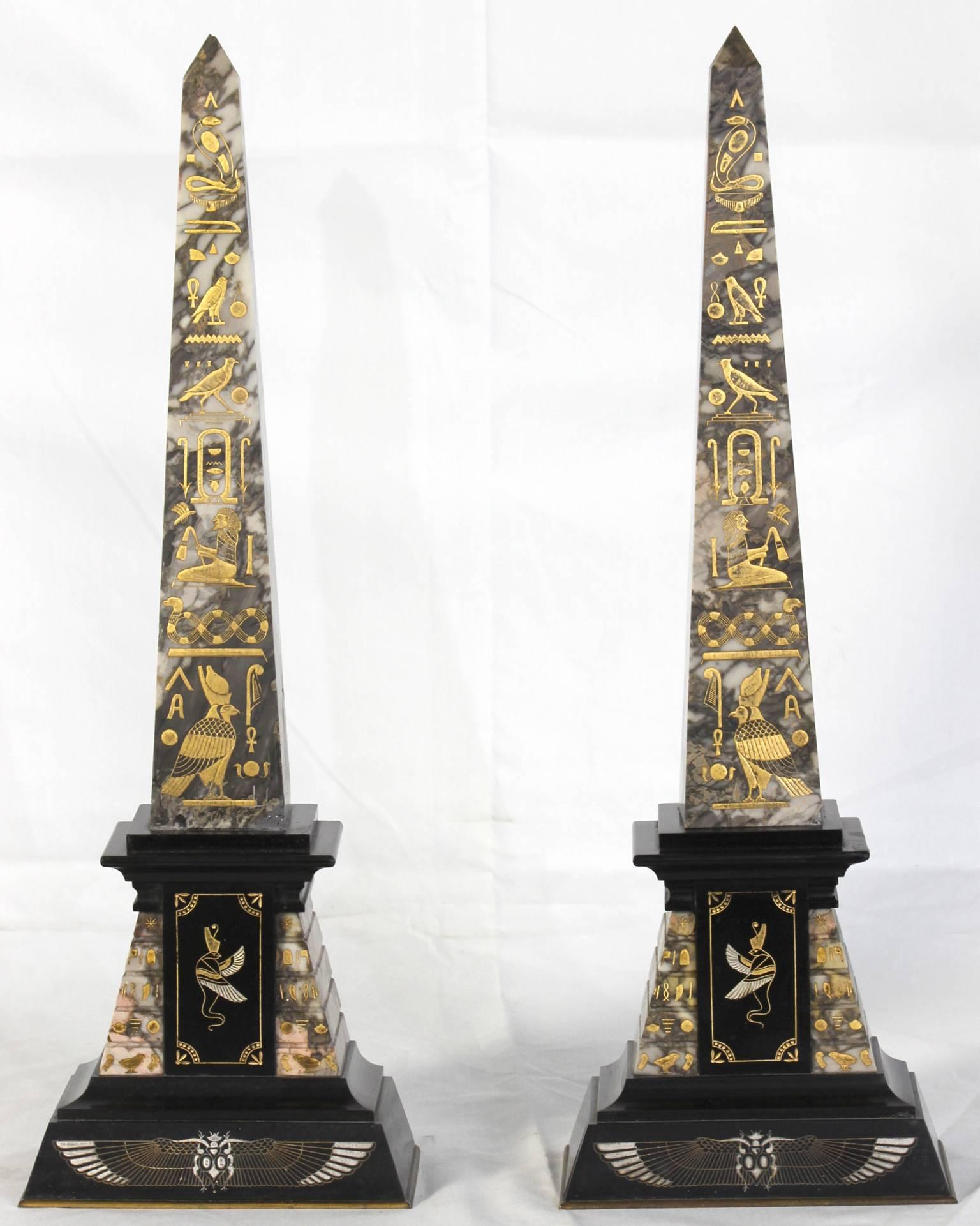 A pair of late 19th century grey marble Egyptian Revival obelisks with incised faux hieroglyphics to front accented in gold and silver enamel on a tiered base accented with black slate.