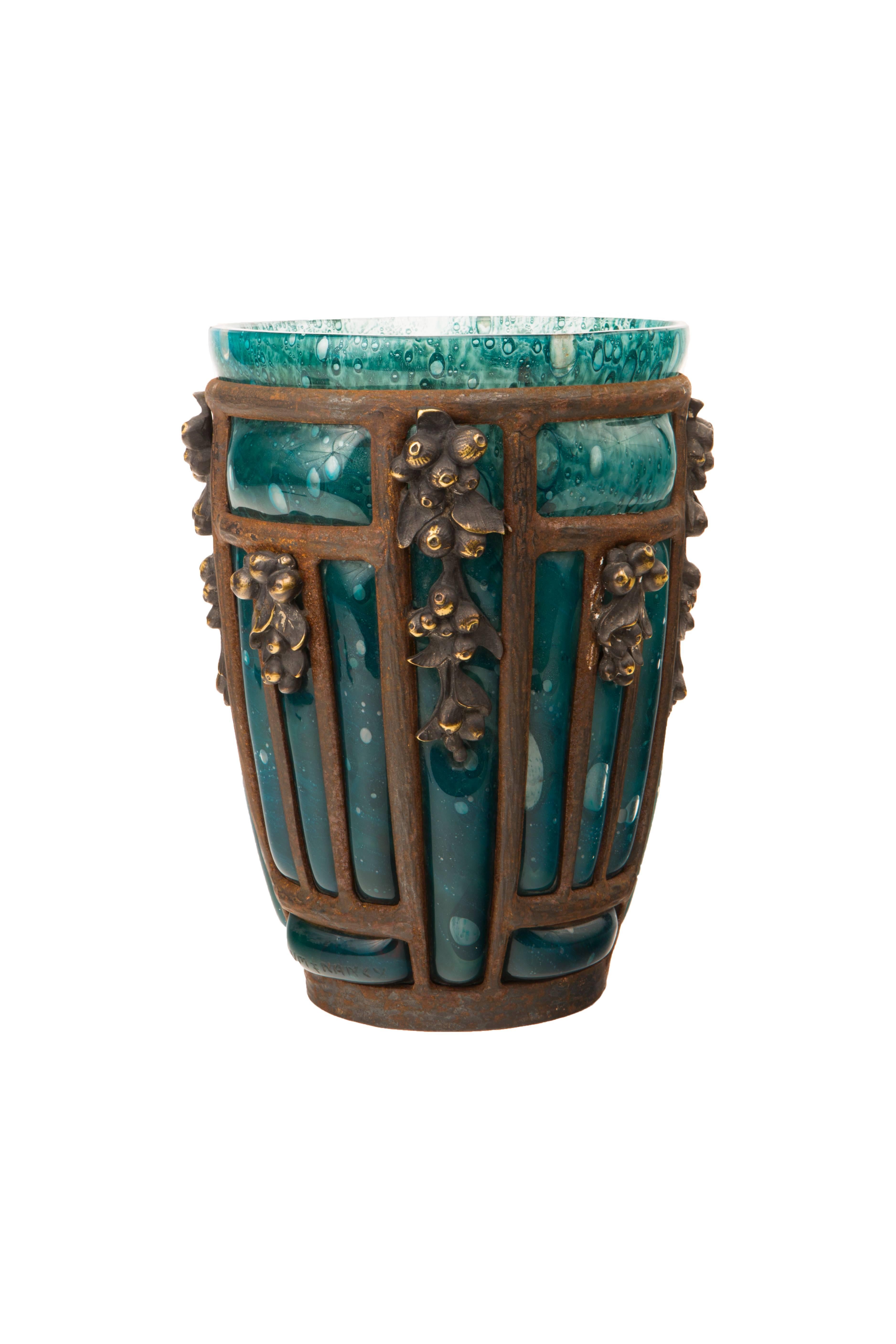 A French Art Deco wrought iron and blown glass vase by Daum Nancy and Louis Majorelle with aqua / green blown out controlled bubble decorated glass blown out with in decorated wrought iron frame further decorated with stylized floral decoration. The