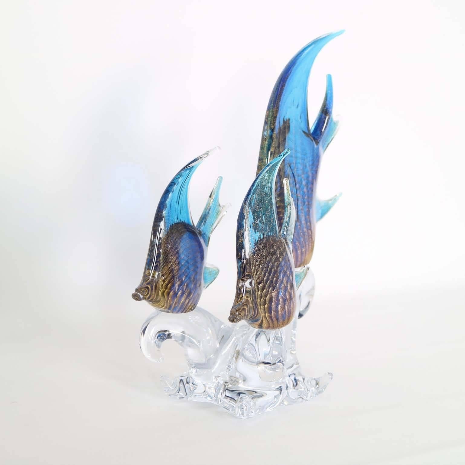 A sculptural trio of blue angel fish, produced in Sardinia, Italy by Marcolin, on a clear wave-form base in lead crystal, each fish with brilliant ripples of gold flakes (cordonato d'oro), mimicking scales. Markings include signature and date to the