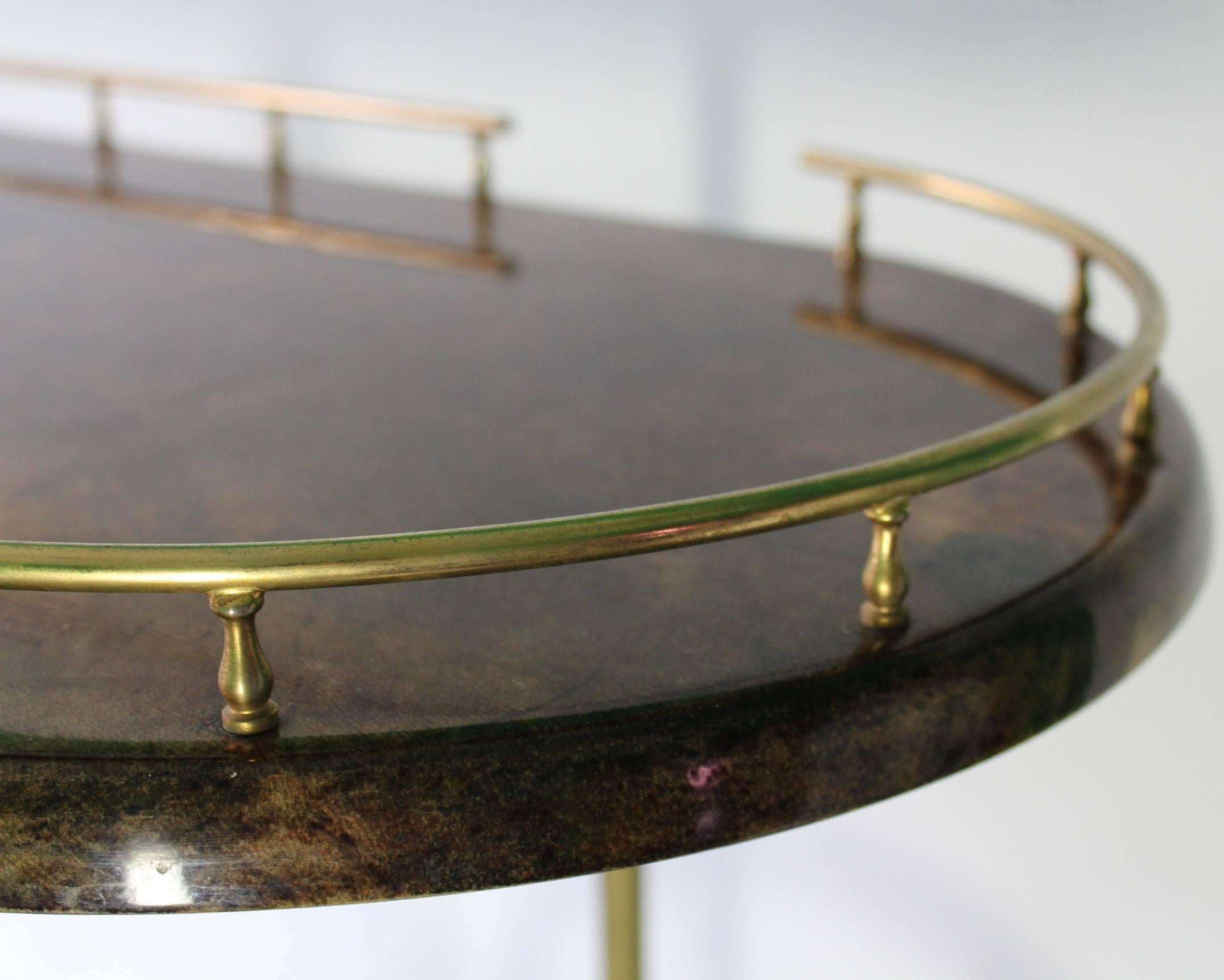 An Italian service and bar cart by Aldo Tura, produced circa 1950s, with two rounded tiers in brown lacquered goatskin, each with brass galleries, the top with scrolled push handle, the bottom with three bottle holders on spoke wheels, separated by