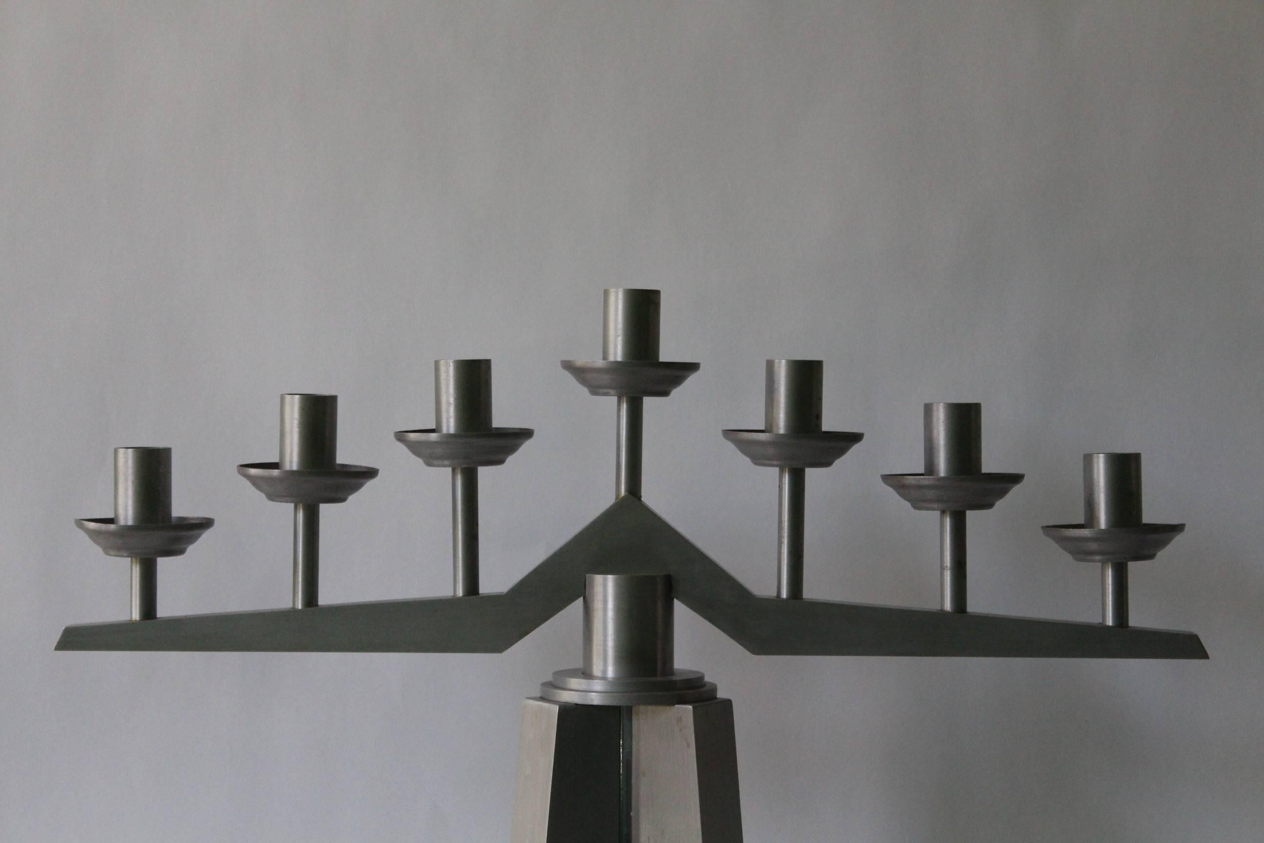 A candelabrum in the Art Deco style, produced in the United States, circa 1940s, in brushed aluminum, with linear arms, supporting seven raised lights and round bobeches, on angular shaft and circular base. Very good vintage condition, wear and