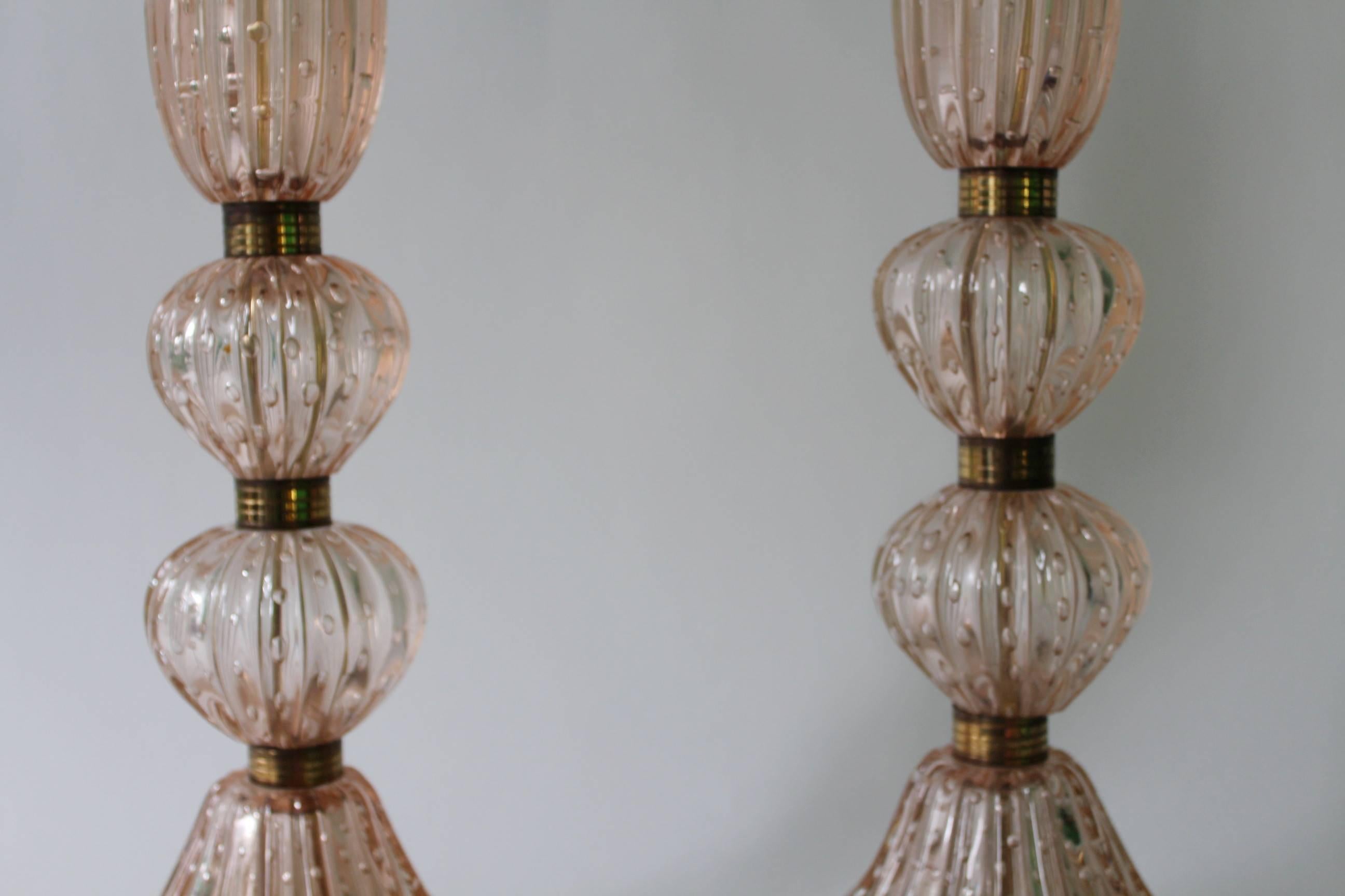 Pair of circa 1950s table lamps in Murano glass by Barovier and Toso, each with single socket on ribbed, baluster form pink glass bodies with controlled bubbles (bullicante) and brass banding, mounted on their original bases. Dimensions provided