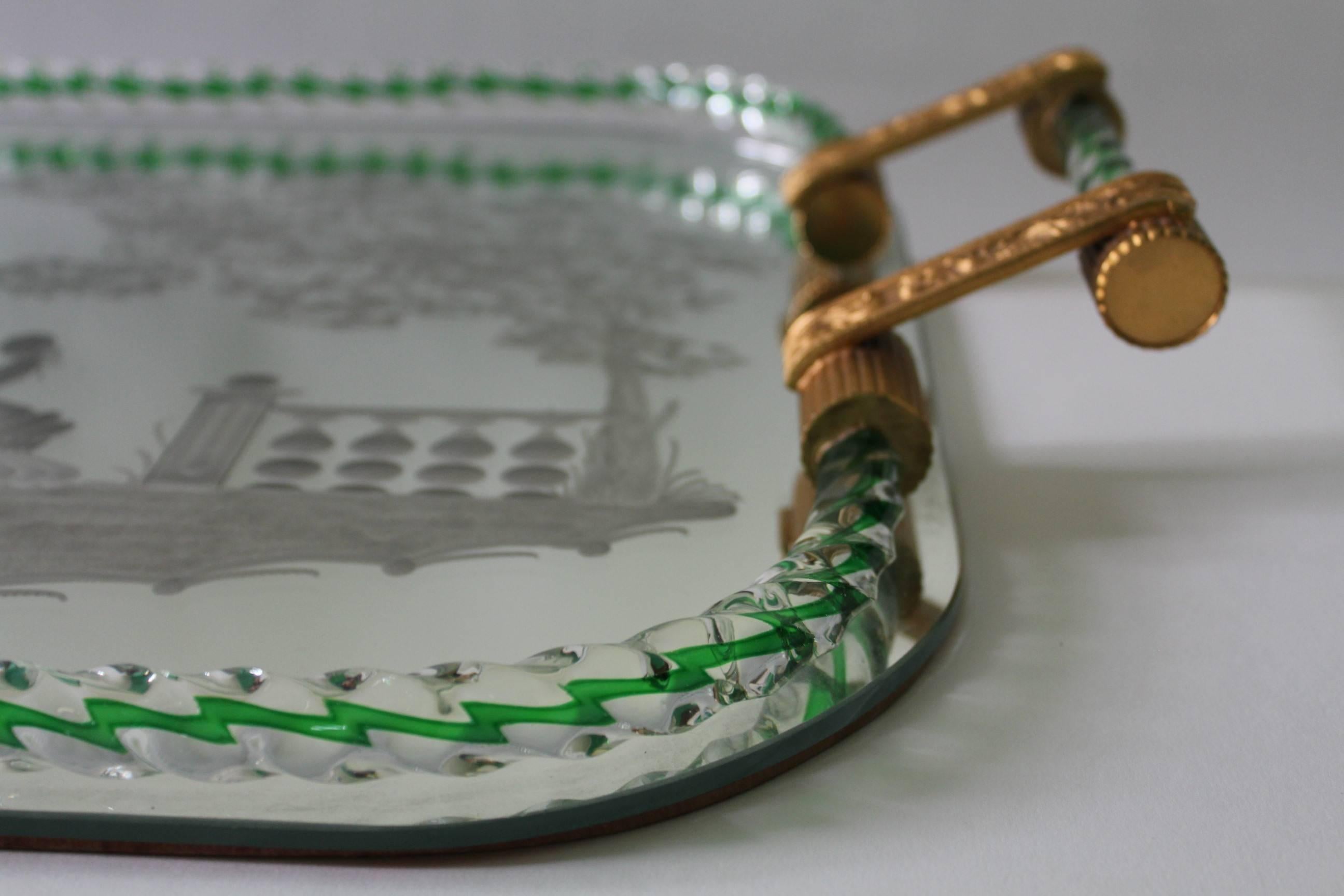  A circa 1940s serving tray with gilt brass handles and twisted Murano glass gallery with green striping, attributed to Arcole Barovier, surrounding a mirrored surface, etched with frosted detail, depicting a garden scene with figures in 18th