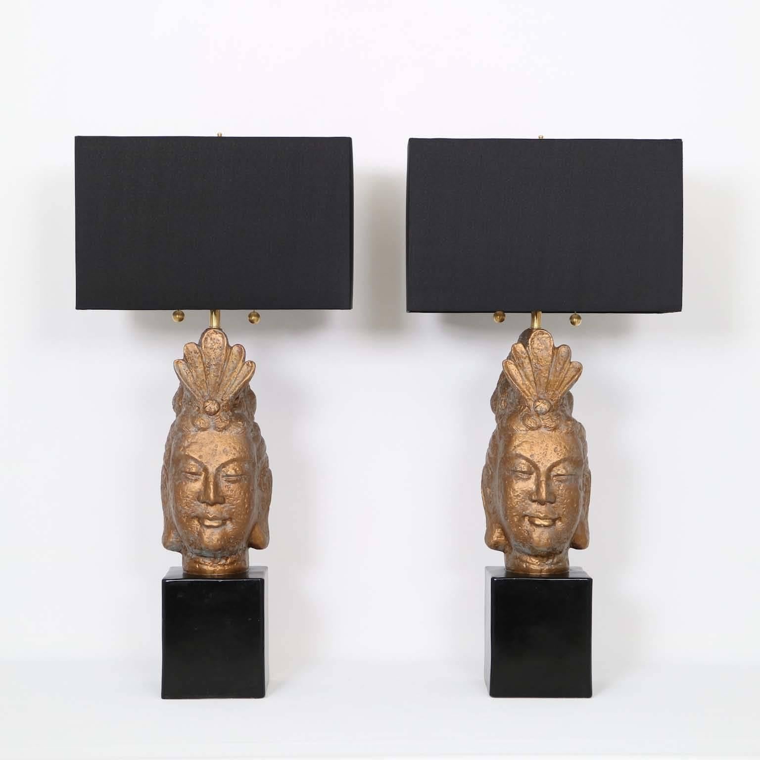 A pair of exotic sculptural table lamps by Quartite Creative Corp., designed in the manner of James Mont, with Buddha heads in plaster, painted in bronze tone, on black bases. Markings include maker name, dated 1959 to the backs. Noted height is to