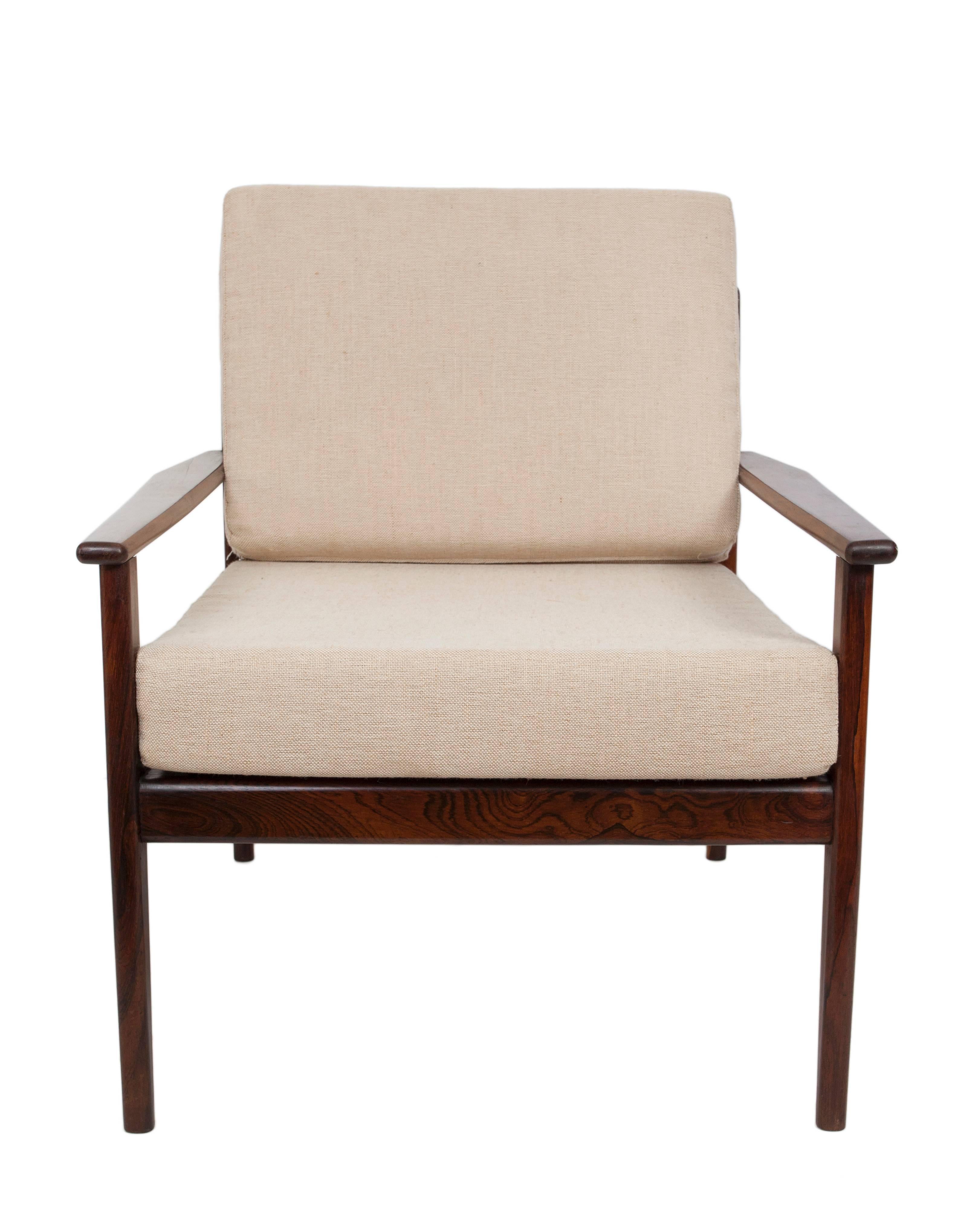 An armchair in the style of Brazilian designer Joaquim Tenreiro, manufactured circa 1960s, with cushioned seat and back against a rich toned wooden frame. Excellent vintage condition, consistent with age and use.