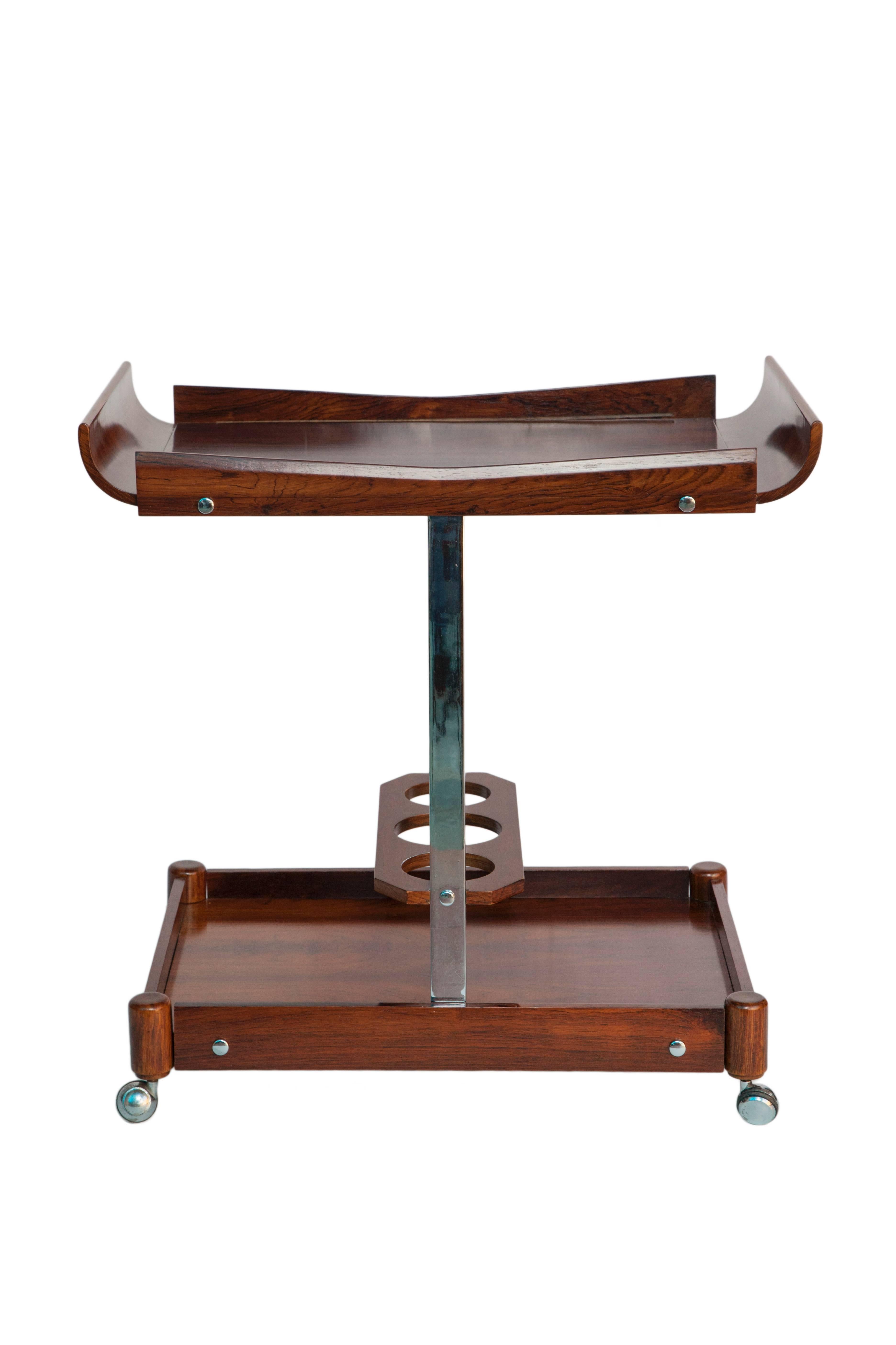 A Brazilian modern rolling bar cart by Novo Rumo, manufactured circa 1960s, including two tiers and lower bottle holder crafted of jacarandá wood, with metal supports on caster wheels. Excellent vintage condition, consistent with age and use.