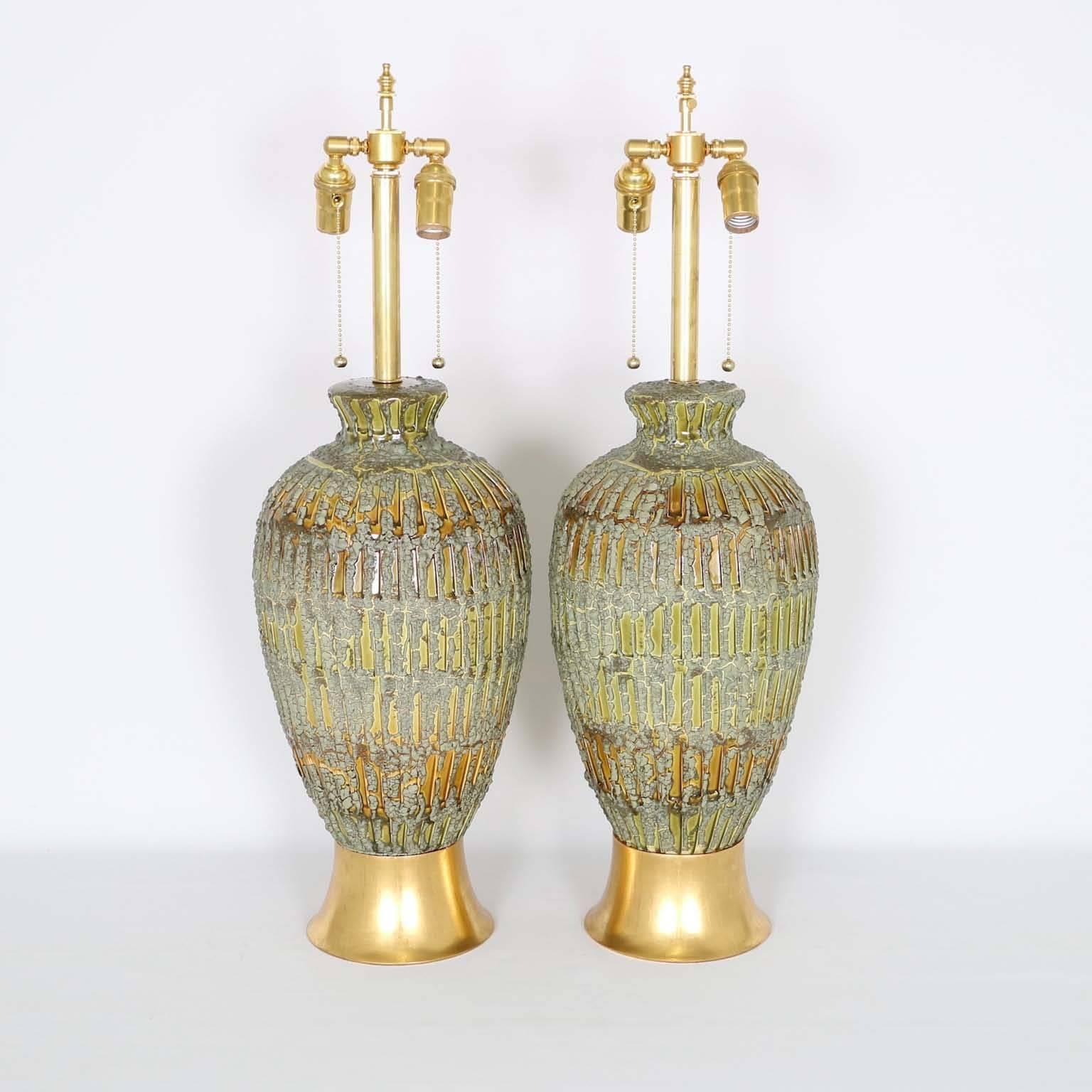 A pair of fantastic Mid-Century Modern drip lava glaze table lamps, produced, circa 1950s, in green-golden tones, the drip lava finish giving the glaze a beautiful dimensional texture. Mounted on gilded wooden bases. The noted height is to the