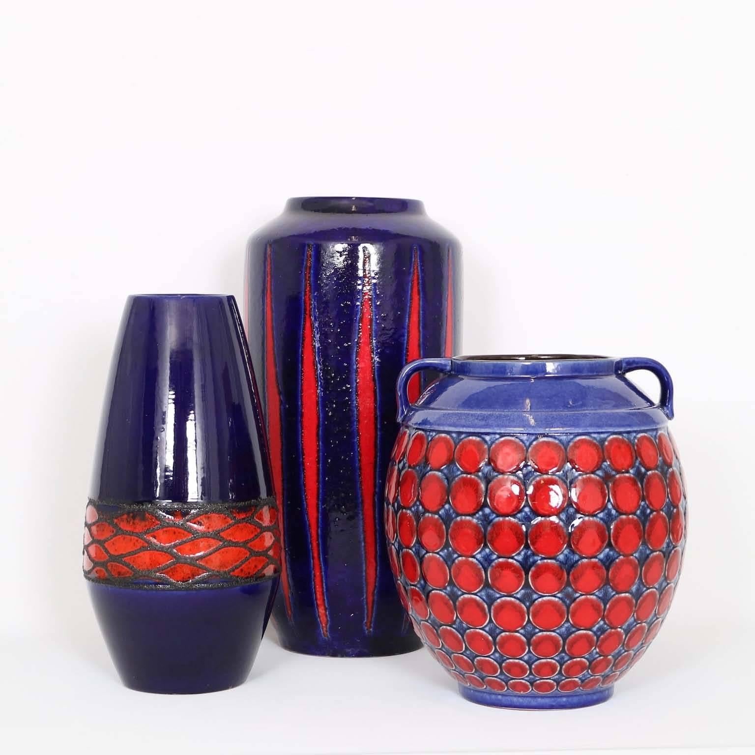 Set of three Mid-Century Modern pottery vases, in colors from navy blue to midnight blue, with red accents. Excellent vintage condition, wear consistent with age and use.

Dimensions of each in descending order:
19” height x 10” diameter.
15.5”