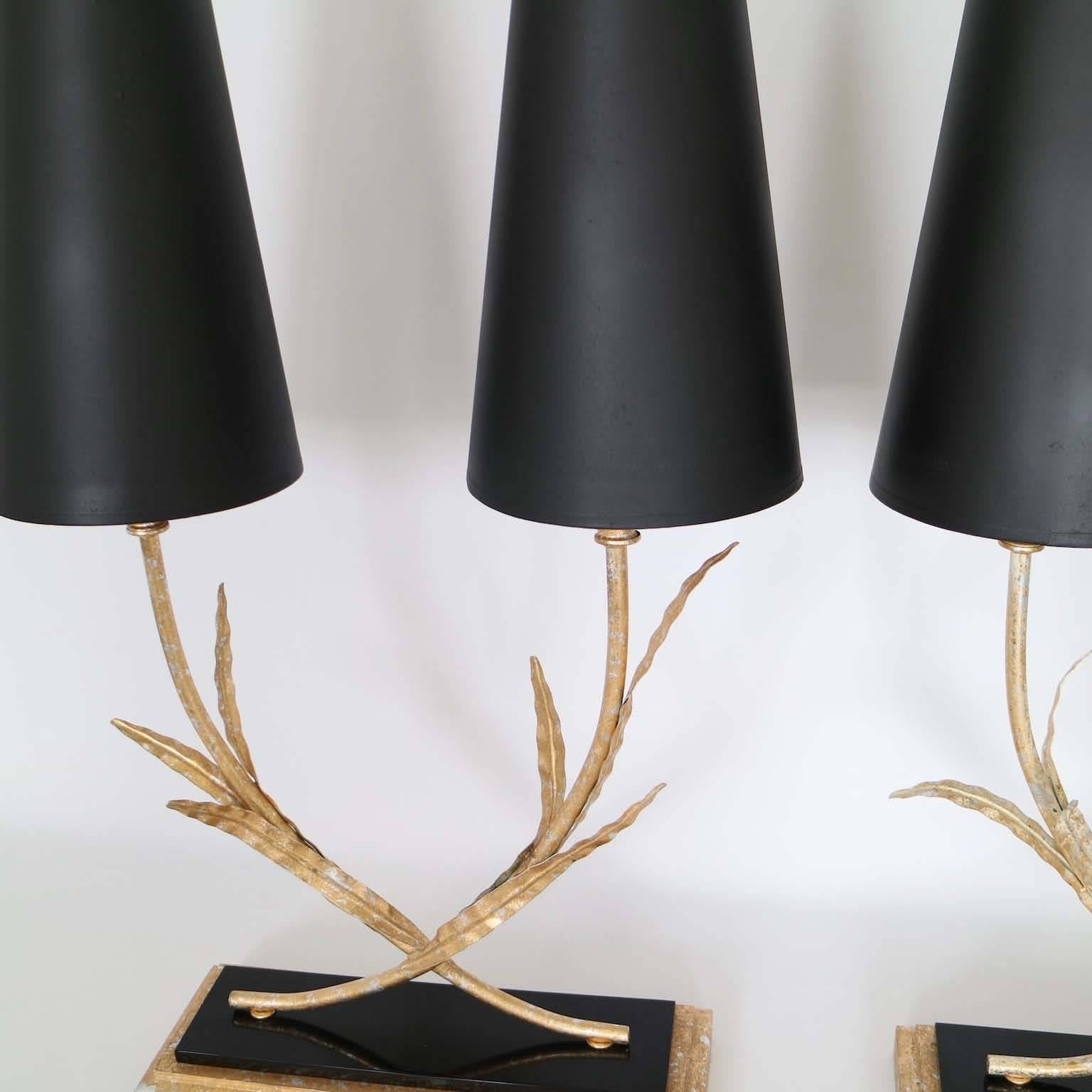 Pair of Mid-Century Modern gilt and plated tole lamps, produced, circa 1950s, each with double socket, mounted on a wood base with black lucite accent; includes black shades. The lamps remain in perfect vintage condition, newly wired. The noted