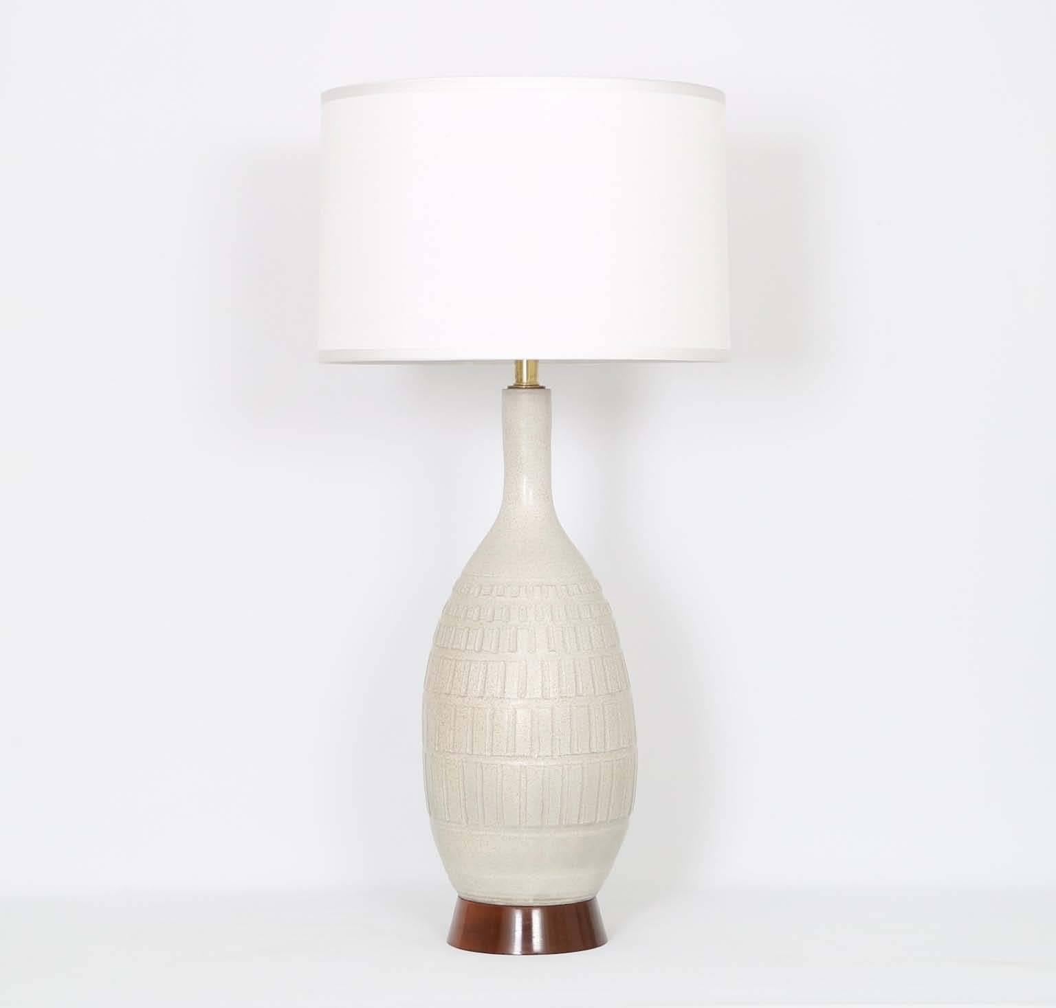 A tall and sculptural studio pottery table lamp by Bob Kinzie, produced, circa 1960s for his company Affiliated craftsmen of California. The earthenware clay body, with an abstract incised design, comes mounted on a solid walnut base. The noted