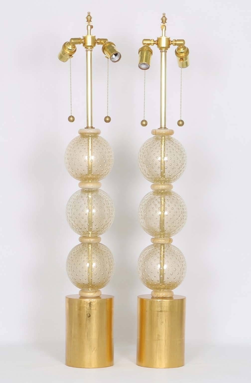 A pair of Hollywood Regency style Murano glass stacked ball table lamps by Barbini, produced in Italy, circa 1950s, with controlled bubbles (bullicante), mounted on gilded wood bases. The noted height is to the finial, height to the top of the glass