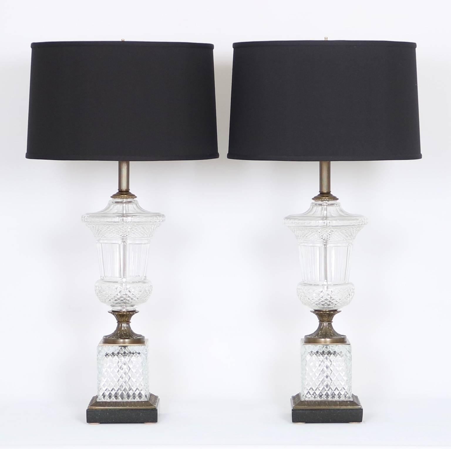 A pair of Hollywood Regency era table lamps, manufactured by Paul Hanson, circa 1950s-1960s, of urn form in faceted crystal, brass mounts with satin finish, on black stone bases. The noted height is to the finial. The height to the top of the socket