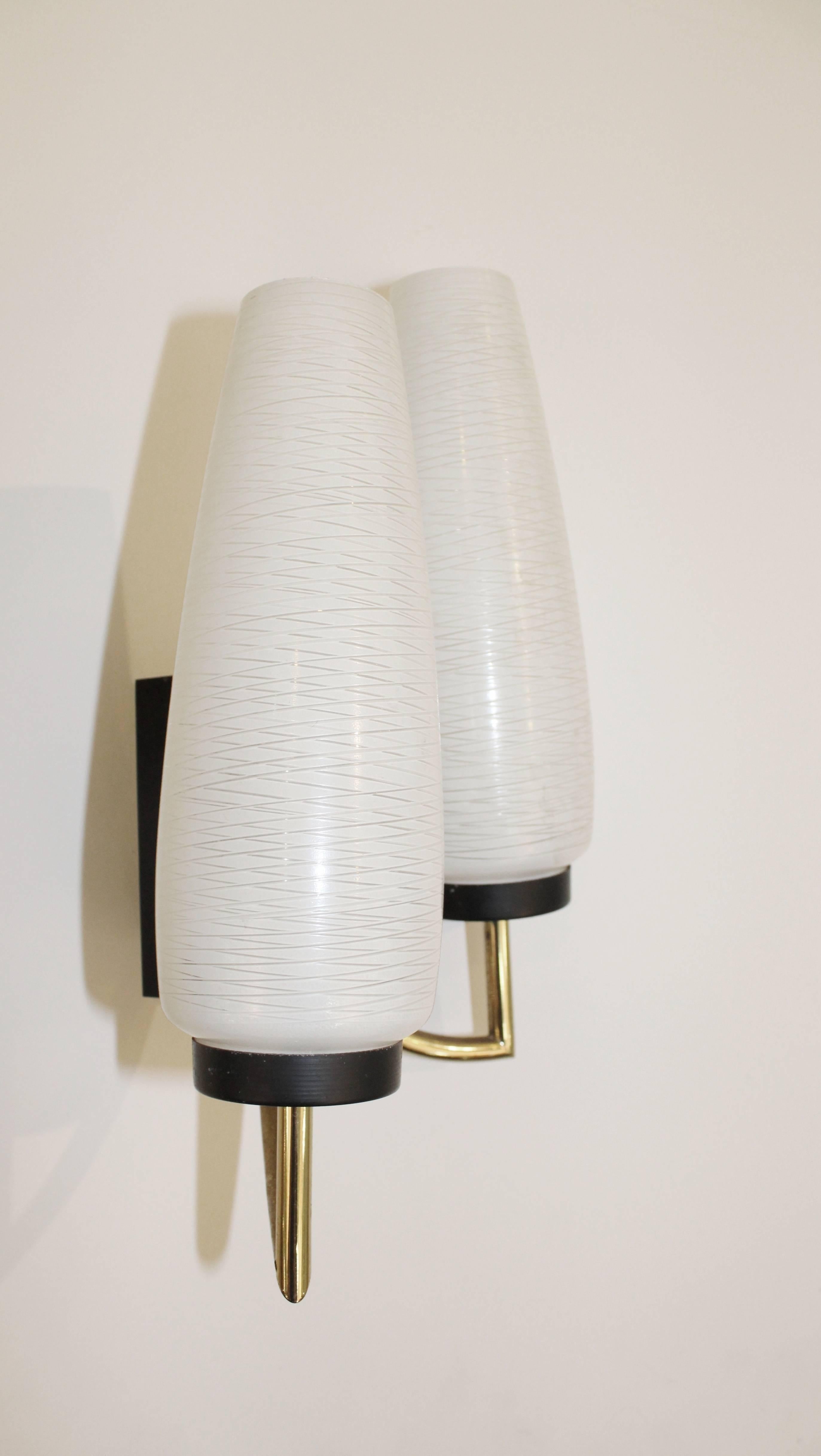A pair of Mid-Century Modern, 1950s dual light wall sconces, featuring white glass tulip shades with decorative incising, on curved brass stems with black enameled accents and back plates. Excellent vintage condition, with age appropriate patina and