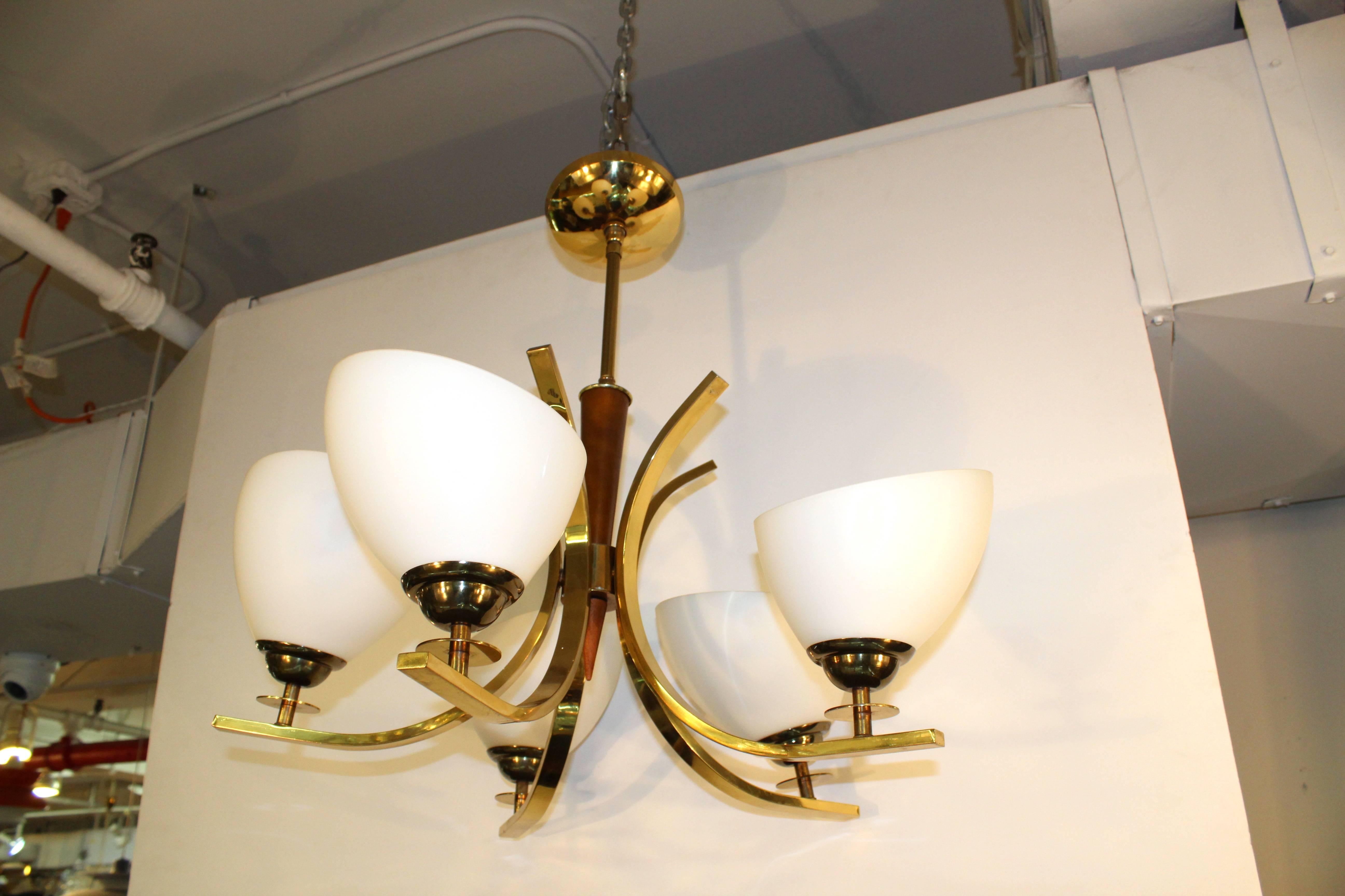 A chandelier with five lights in white opaque glass, polished brass arms and a teak central detail in the Mid-Century Modern style. In excellent condition, with age appropriate wear.

110176.