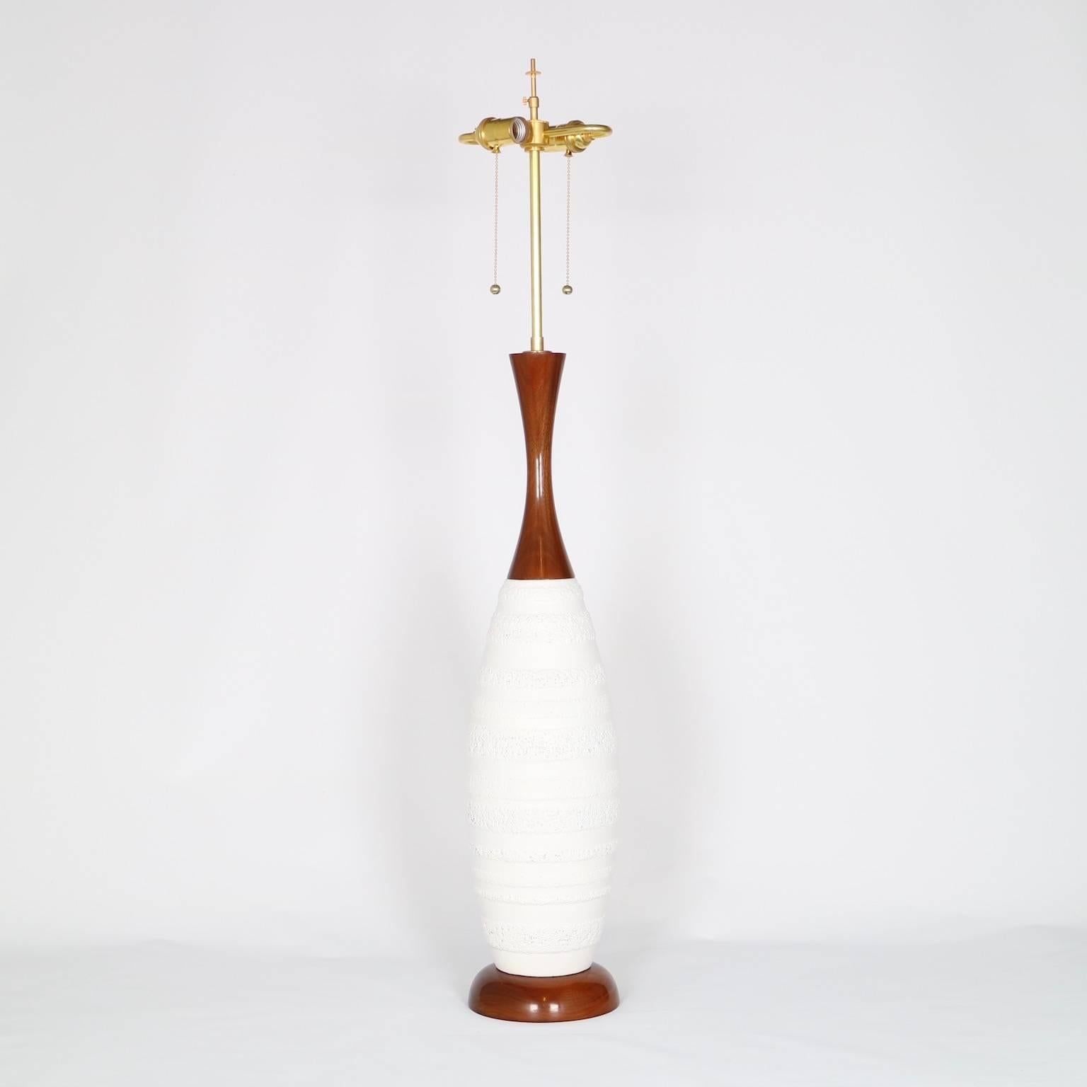 This very tall white ceramic and teak wood baluster table lamp is the most notable of Mid-Century Modern style. The noted height is to the finial. The height to the top of the body is 30 in (76 cm). Excellent vintage condition, fully restored with