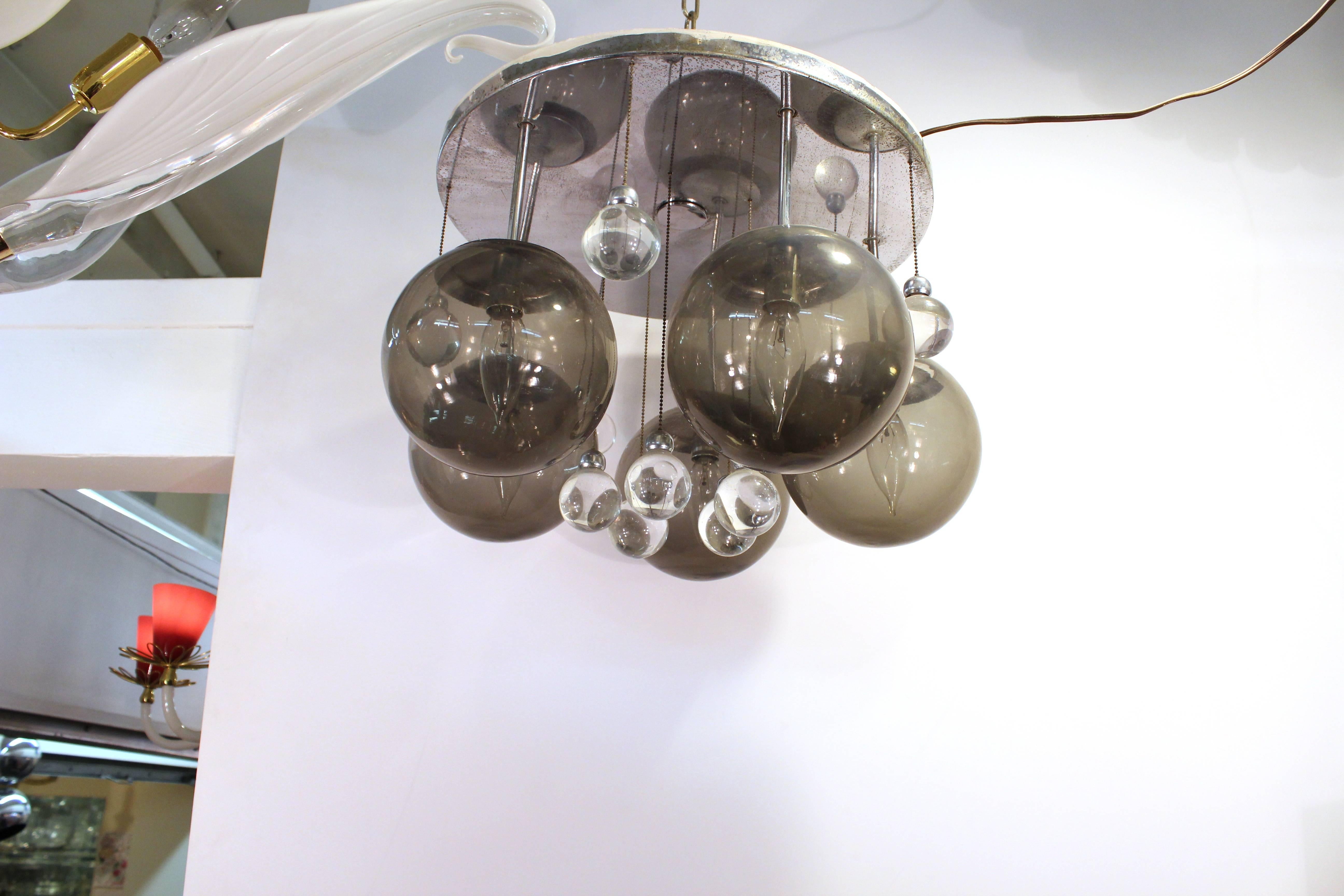 A Mid-Century Modern chandelier in chrome and glass. Comprising of five large smokey glass balls with four smaller clear sphere accents, five matching glass spheres dangle slightly below. All hang from a sleek chrome base. 

 
