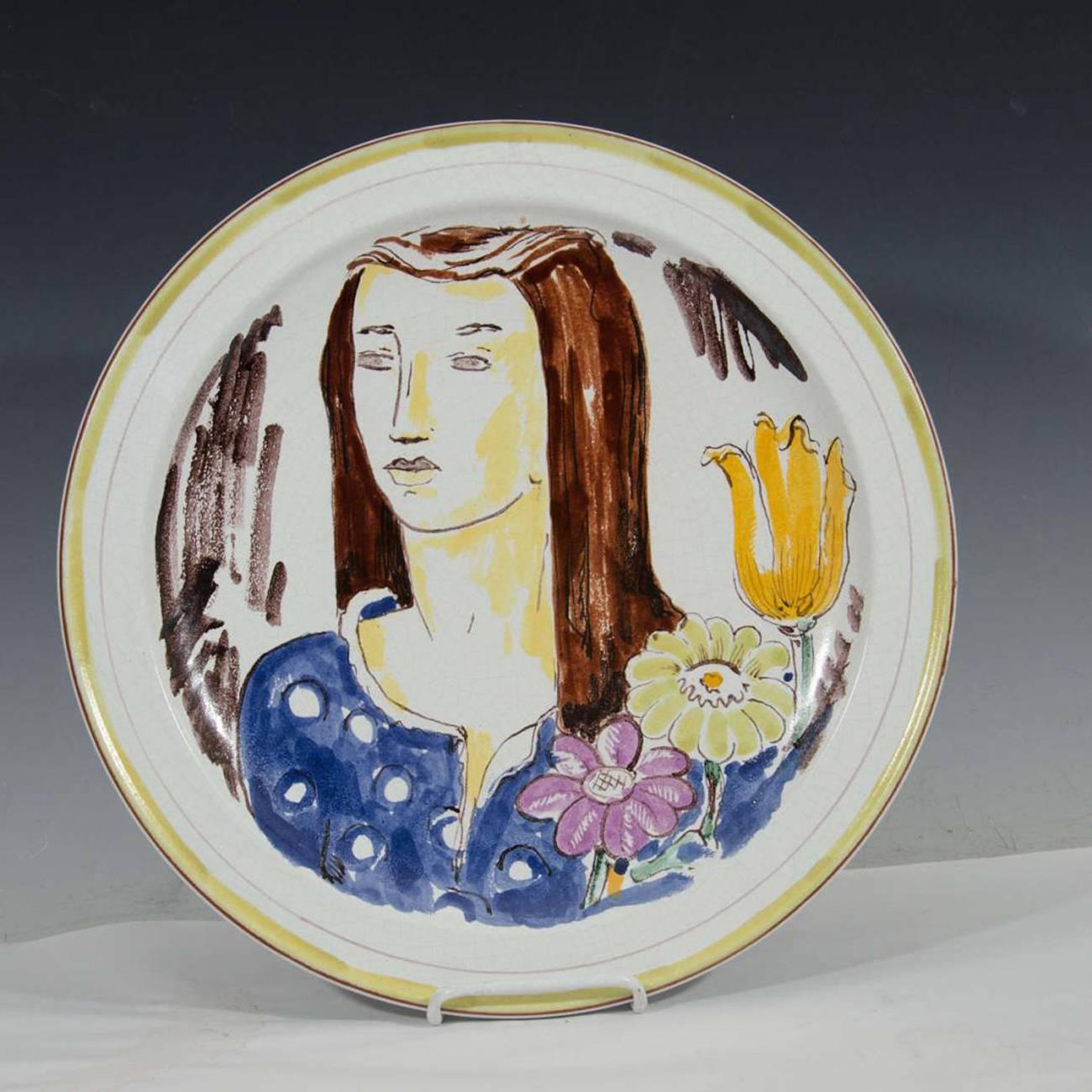 A Mid-Century Wilhelm Kage ceramic plate with a portrait of a woman with flowers. Marked on the reverse.

110338.
 