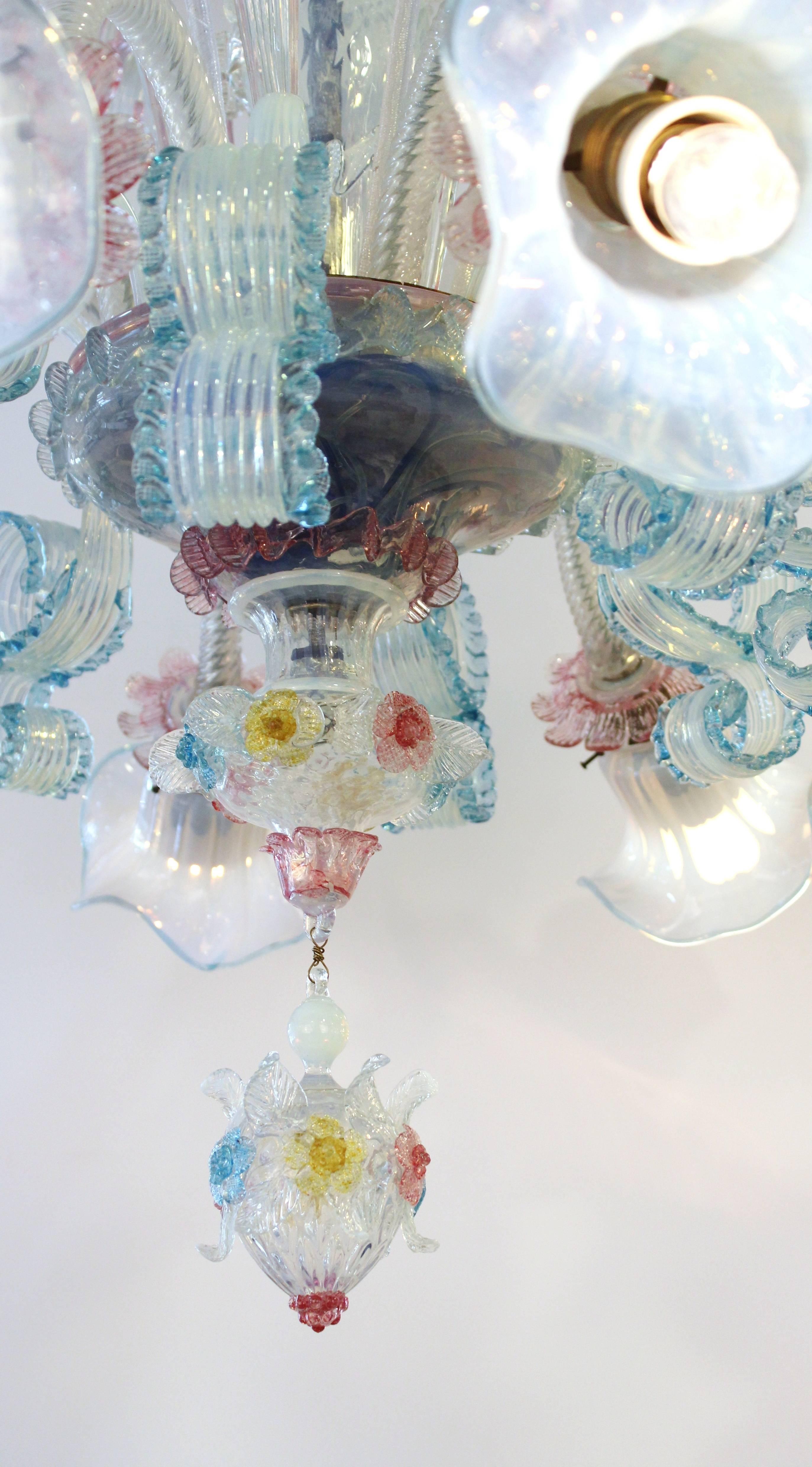 Venetian Murano blown glass chandelier, produced 19th century, featuring floral motifs and decorative scrolls in pale opaline with pink, yellow and blue accents, eight arms terminating in lily form shades. Wired to US standard. Excellent antique
