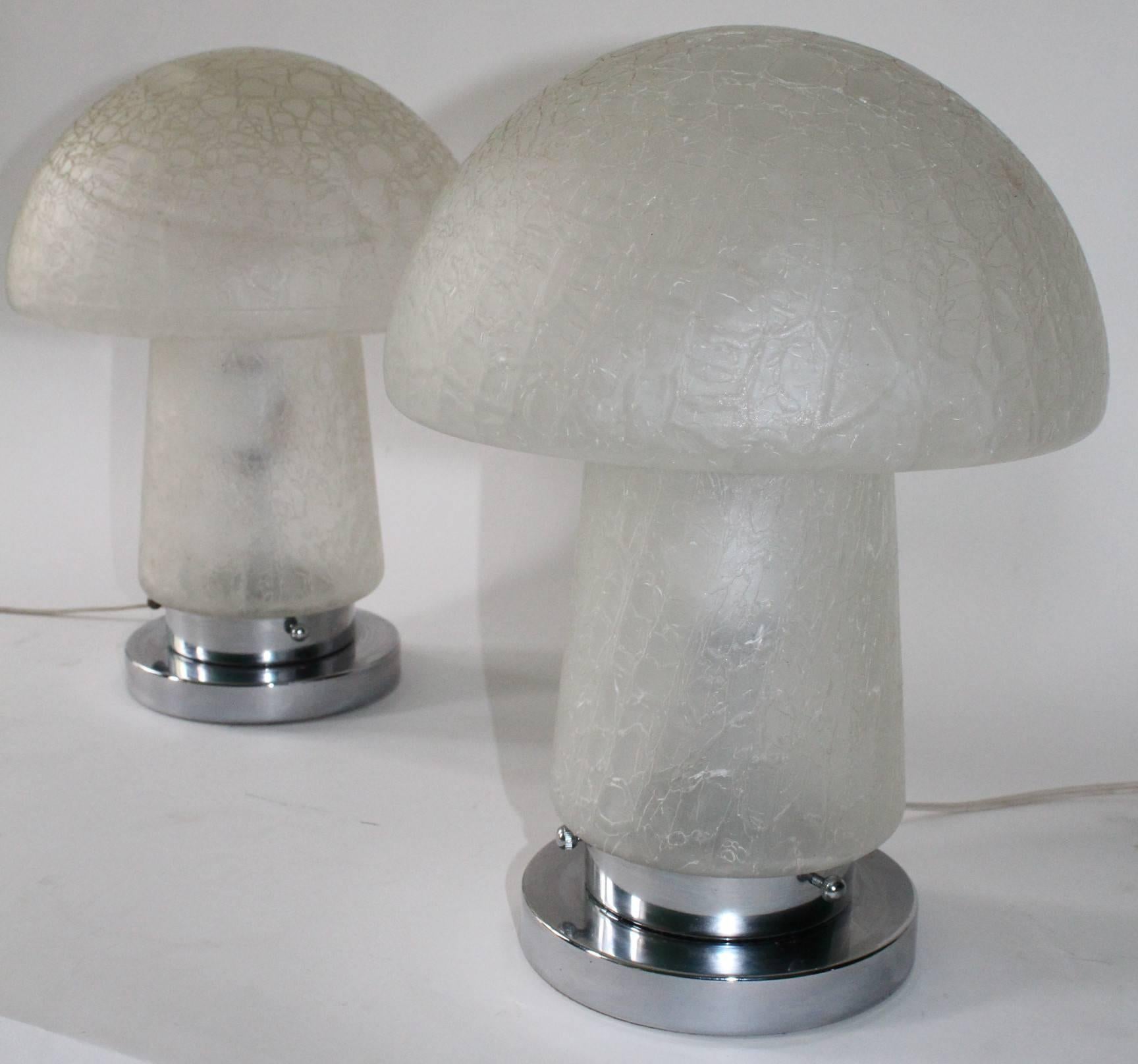 These crackle murano glass mushroom shade lamps from circa 1970 are mounted on polished chrome bases. There is a visible bulge line across one of the lamps on the top which is a natural occurrence sometimes that happens during the blowing