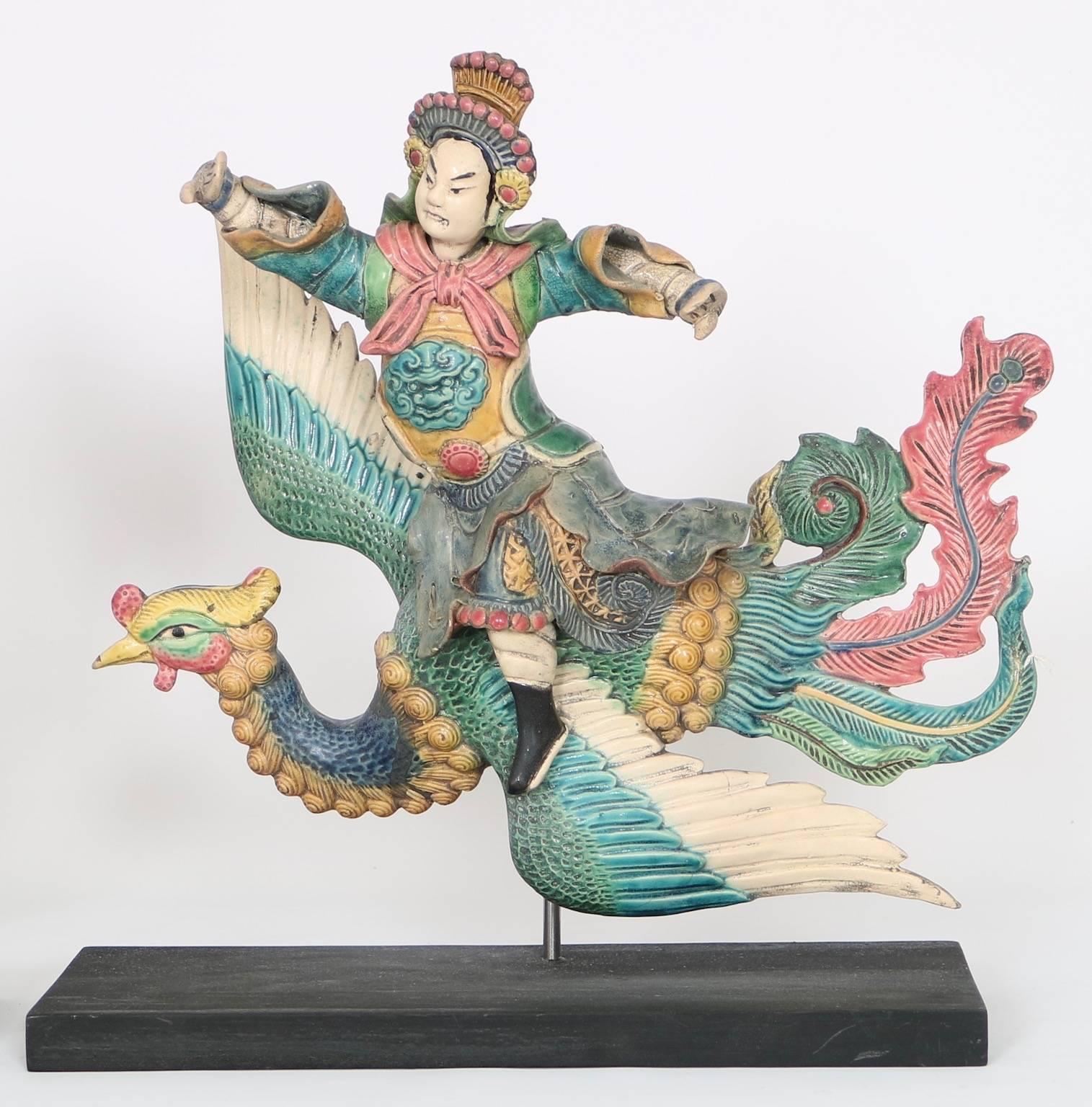 Matching pair of antique early 20th century Chinese roof tiles, crafted of glazed ceramic, depicting warrior characters astride phoenixes riding on the wind, mounted on ebonized wood bases. Excellent condition, wear consistent with age.

110536